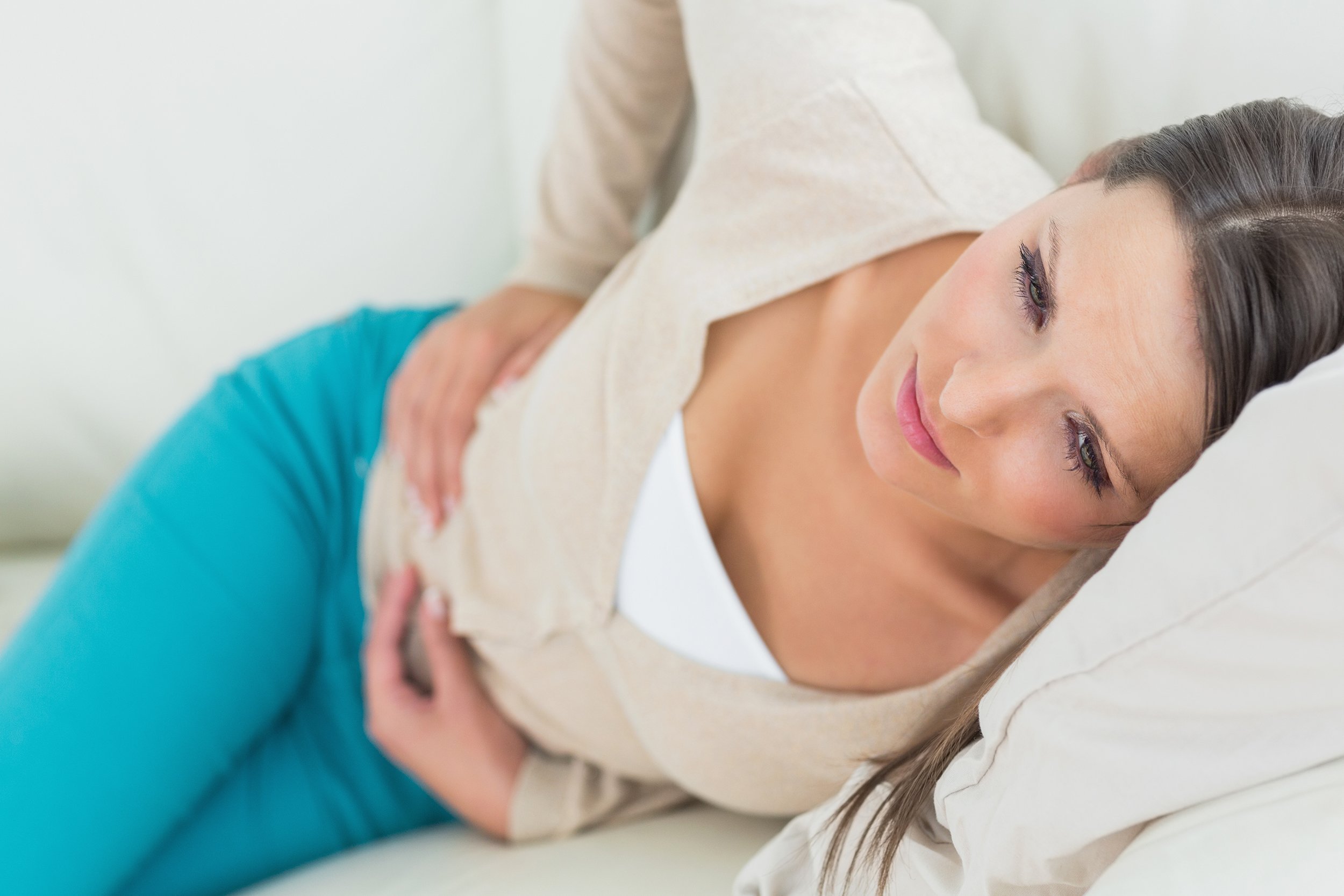 woman lying on sofa looking sick with stomach ache in the living room