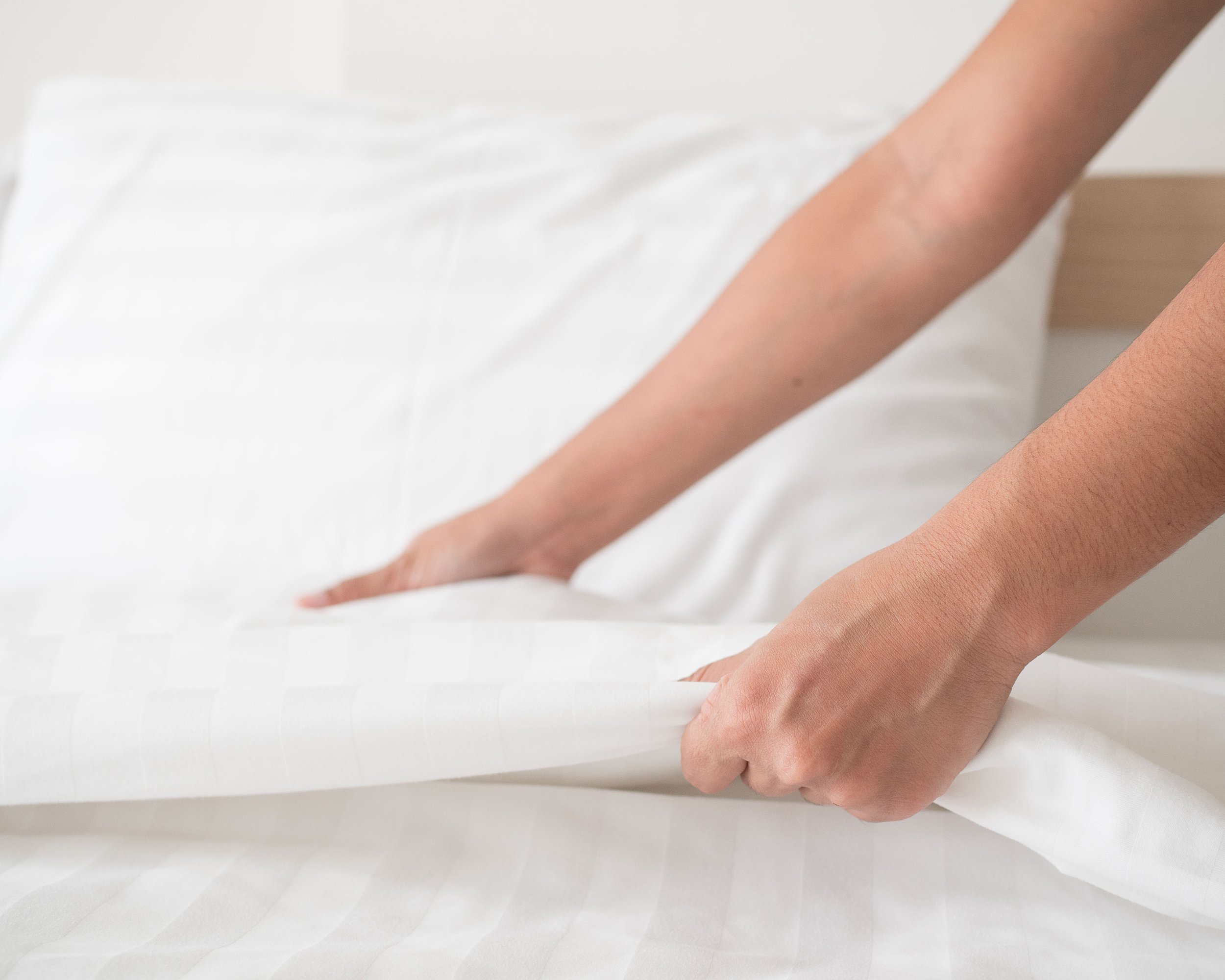 hands making bed of hotel room