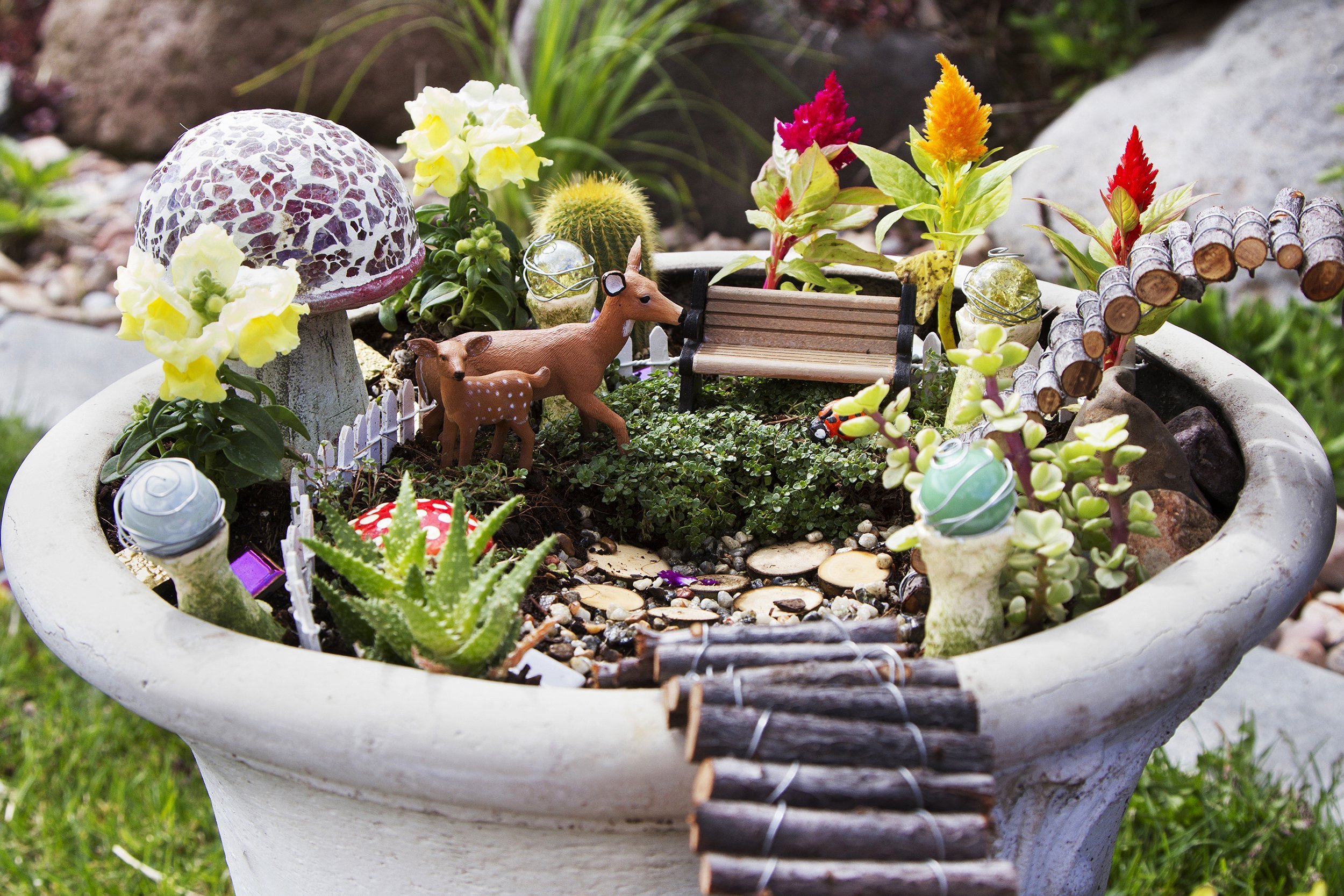 fairy garden with deer, gazing balls and mushrooms in a flower pot