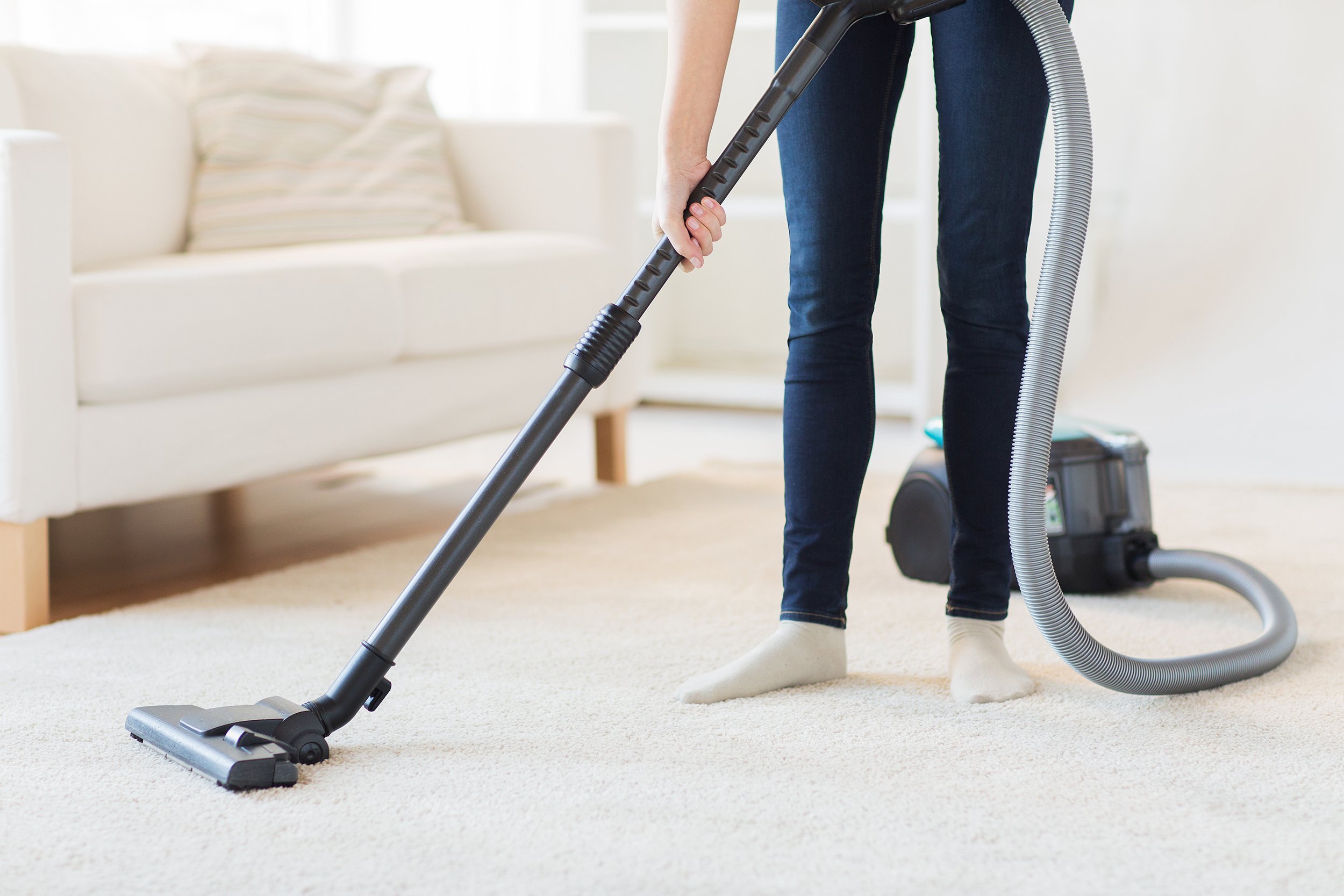 close up of woman with legs vacuum cleaner cleaning carpet at home