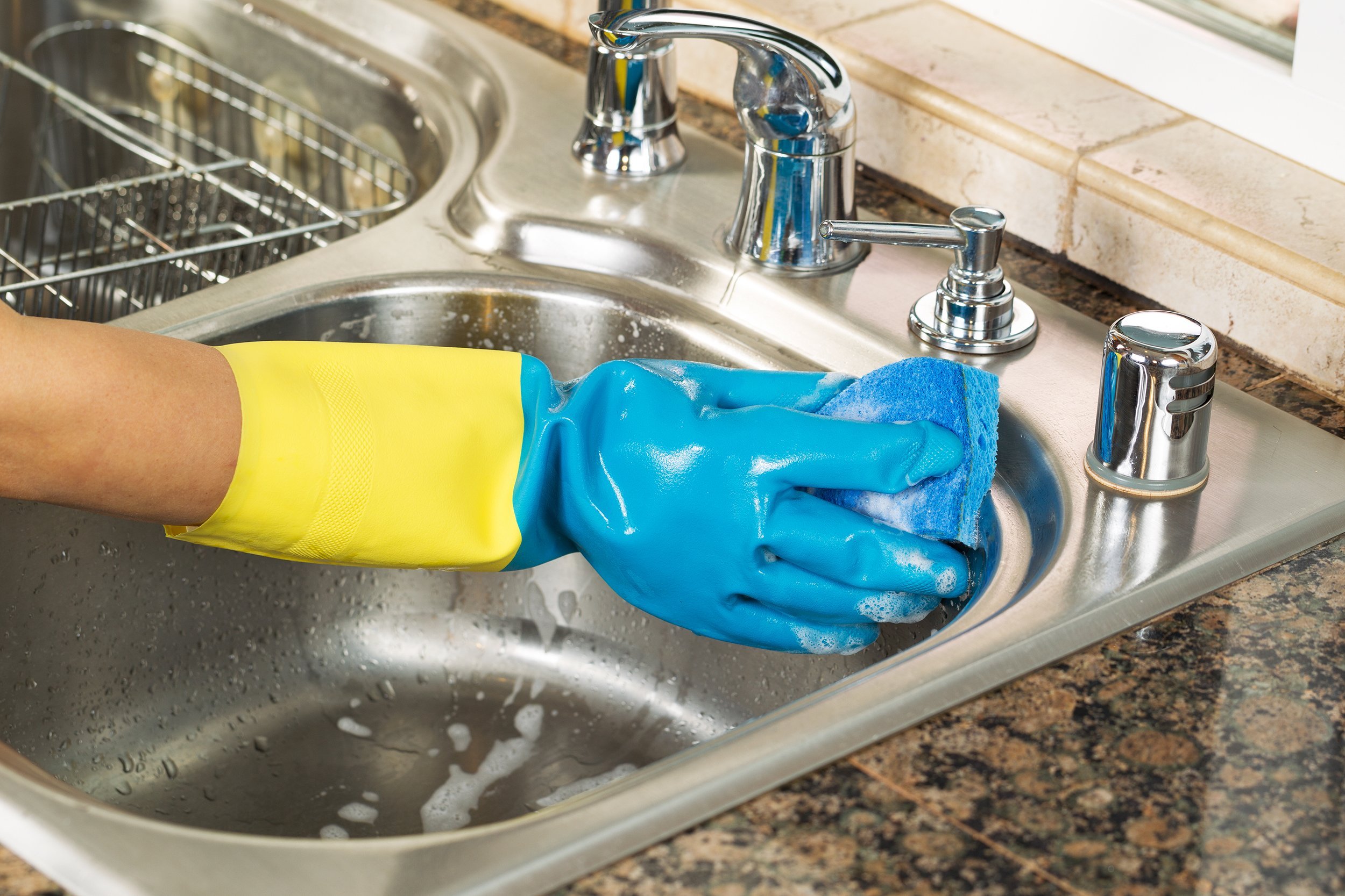 hand wearing rubber glove washing inside of kitchen sink with sponge