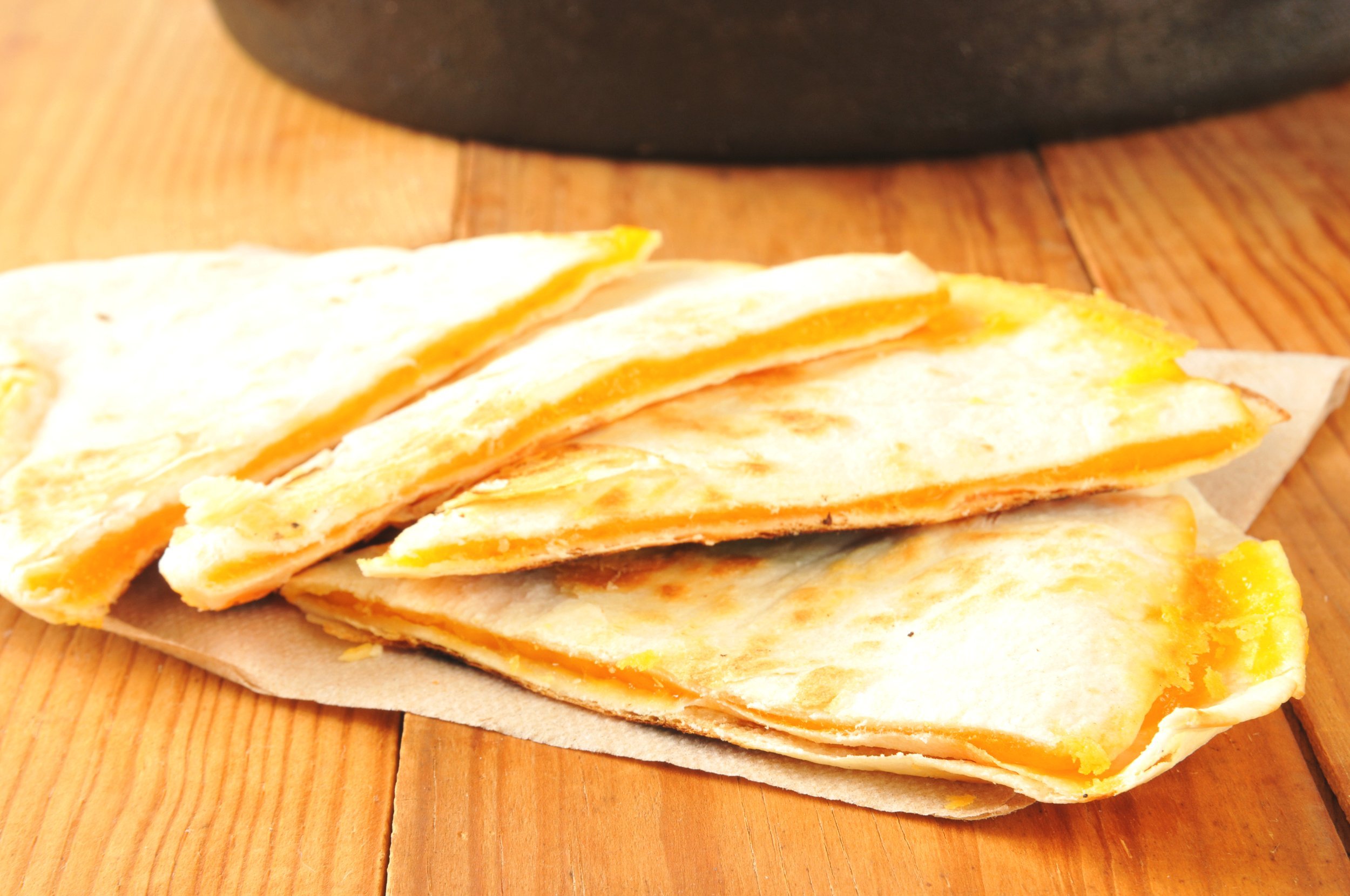 Cheddar cheese quesadillas on a wooden table with a cast iron skillet in background