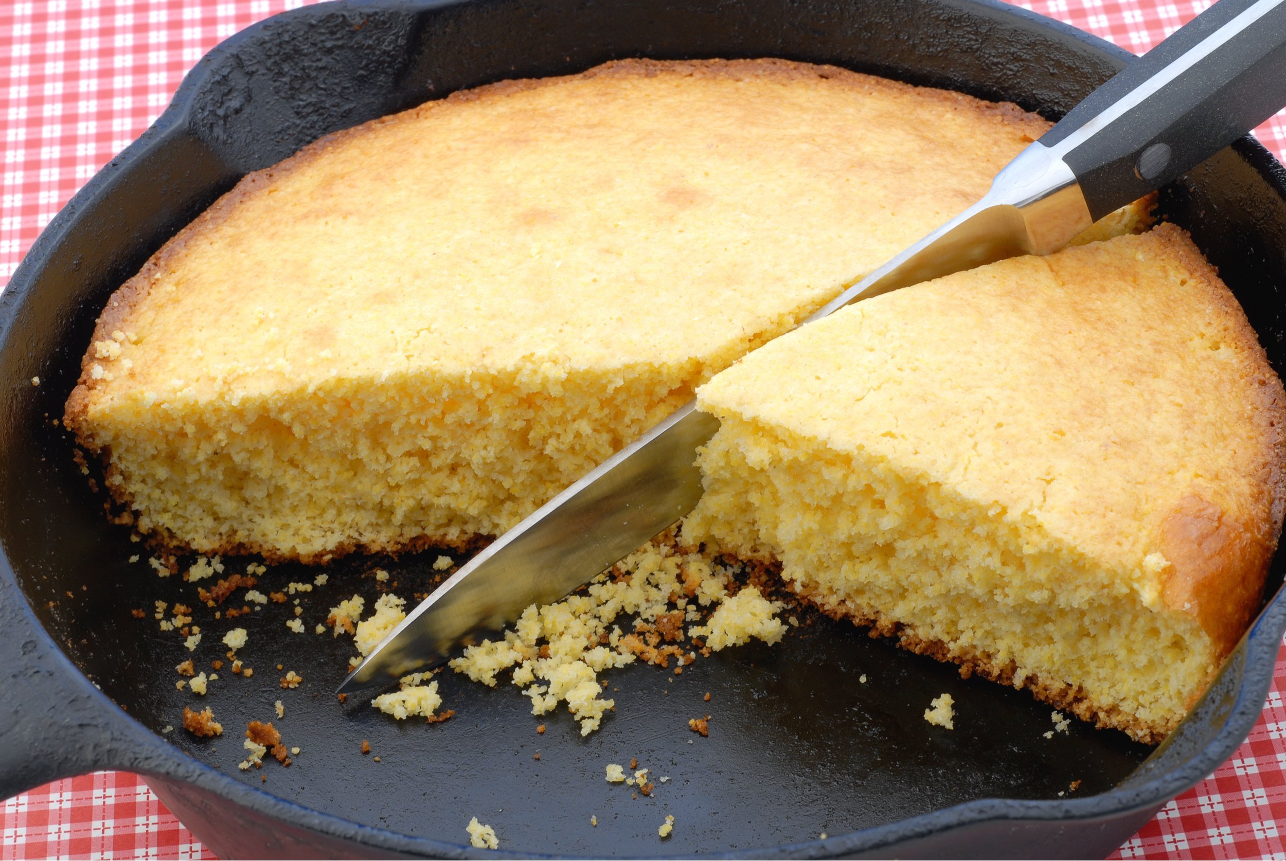 Closeup of cornbread in a cast iron skillet against red checker background