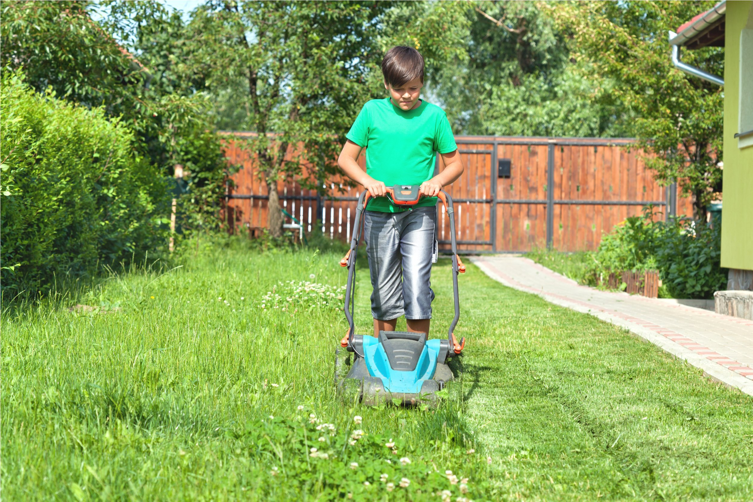 Boy cutting grass around the house in summertime