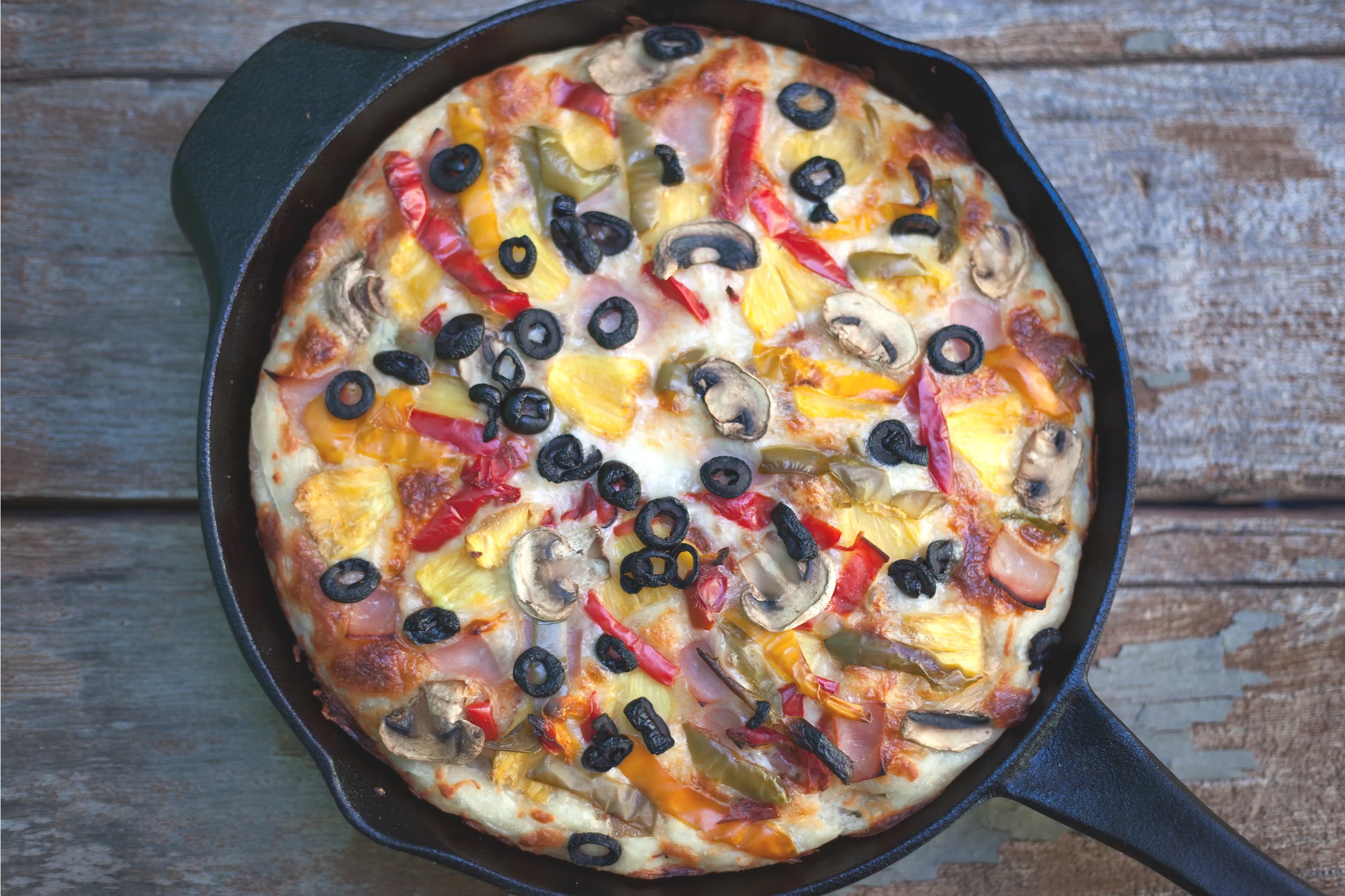 Colorful homemade cast iron pan pizza on vintage wood background
