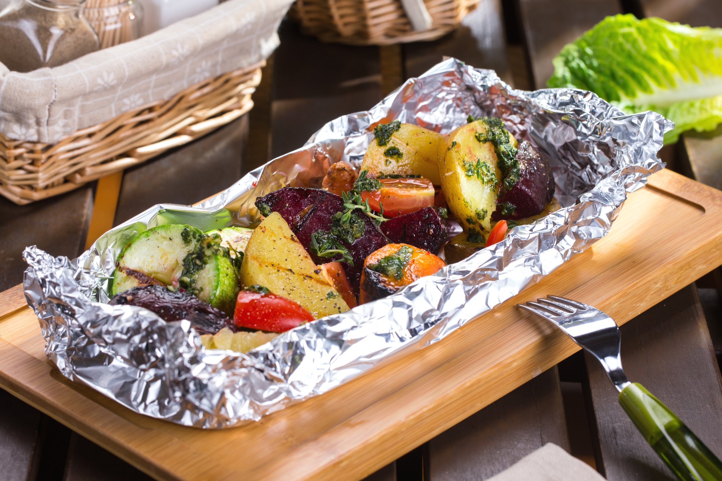 Baked meat with vegetables in foil on wooden table with fork