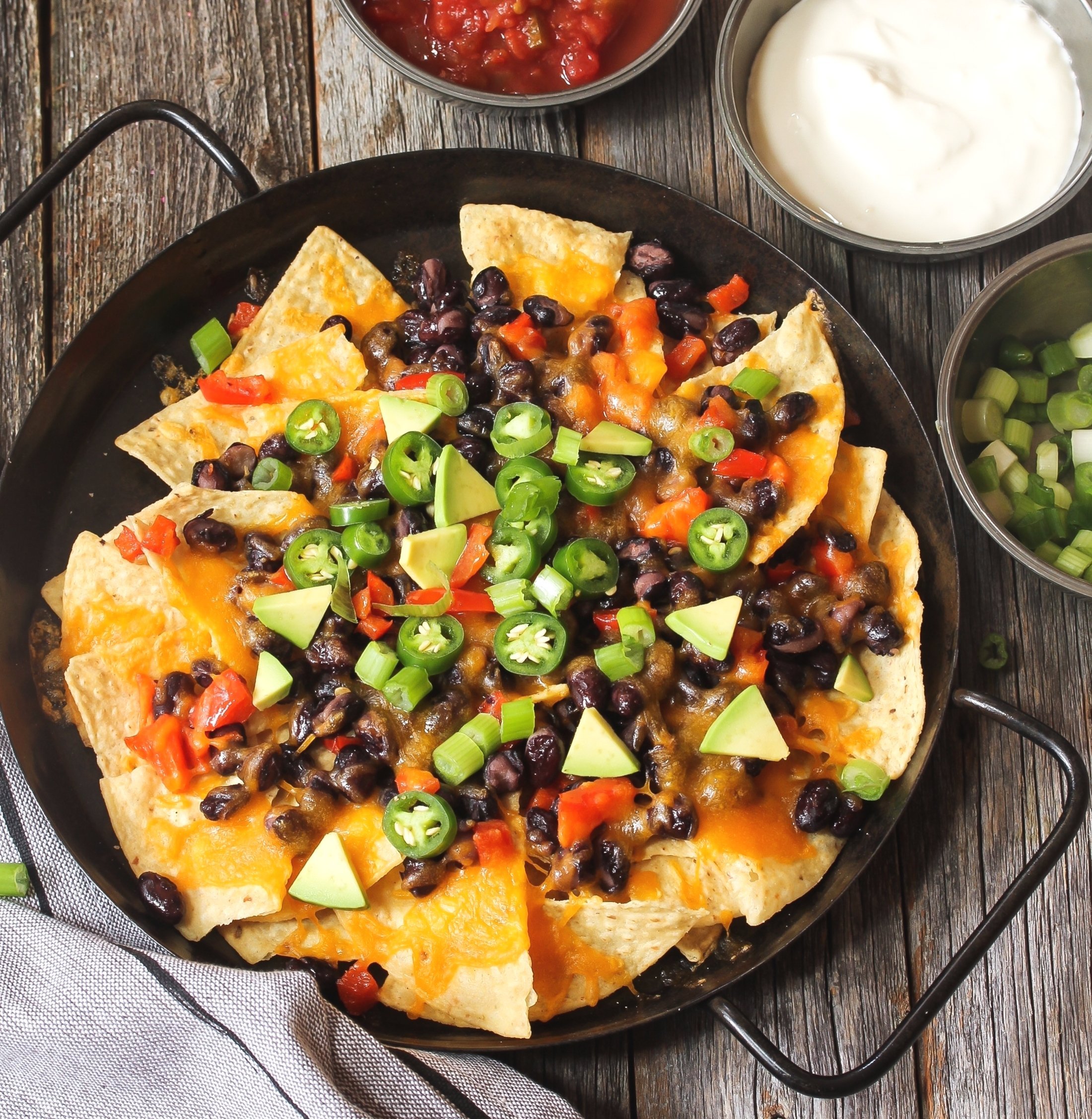 Classic nachos with tortilla chips, melted cheese sauce, jalapeno peppers, avocado, salsa, and sour cream