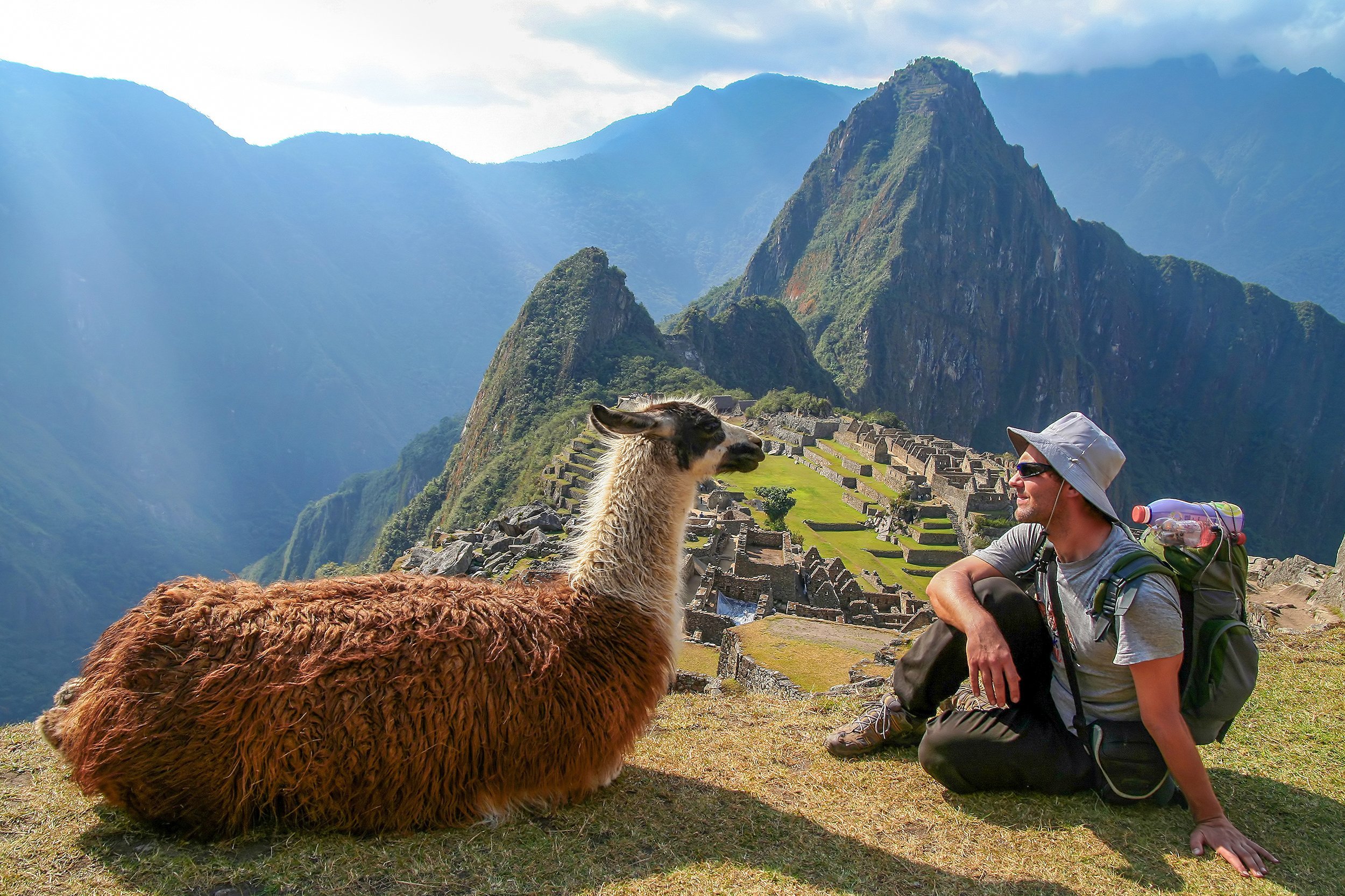 tourist and llama sitting in front of Machu Picchu, Peru