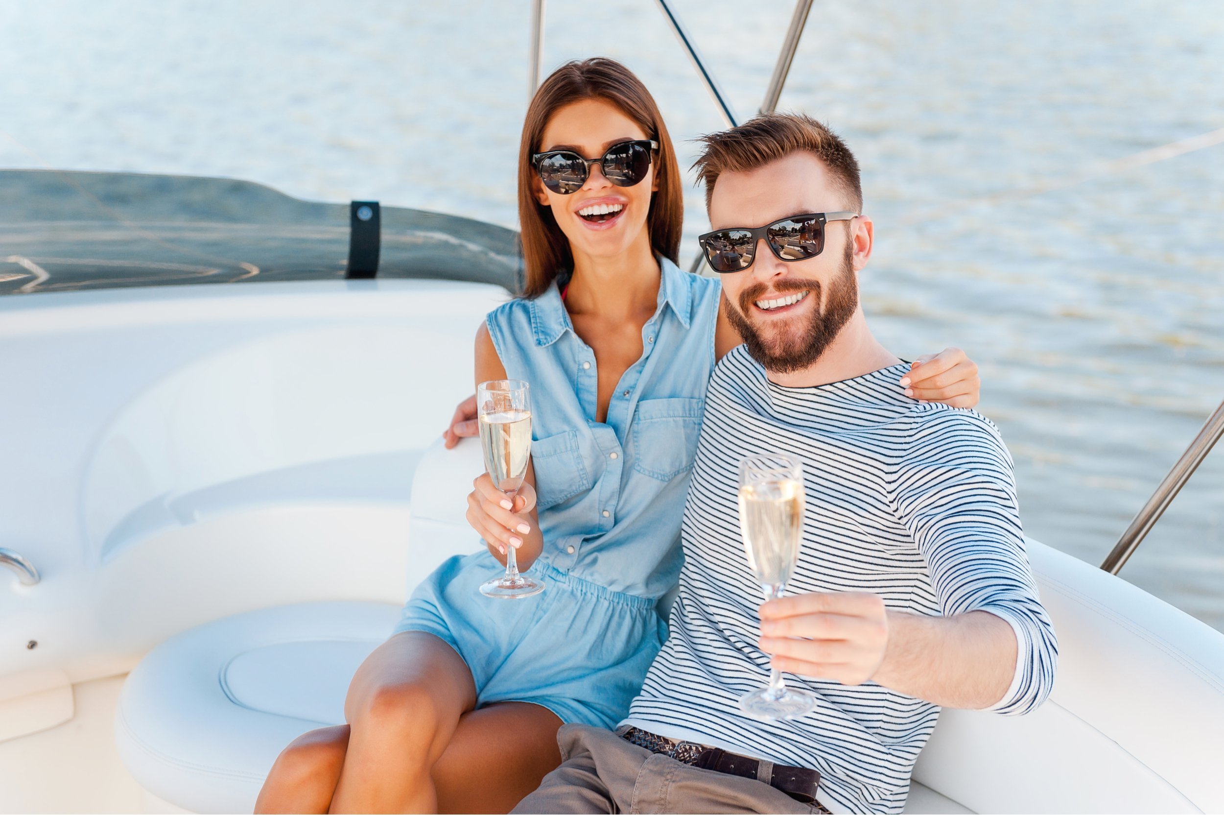 cheerful young couple holding glasses of champagne on the board of yacht