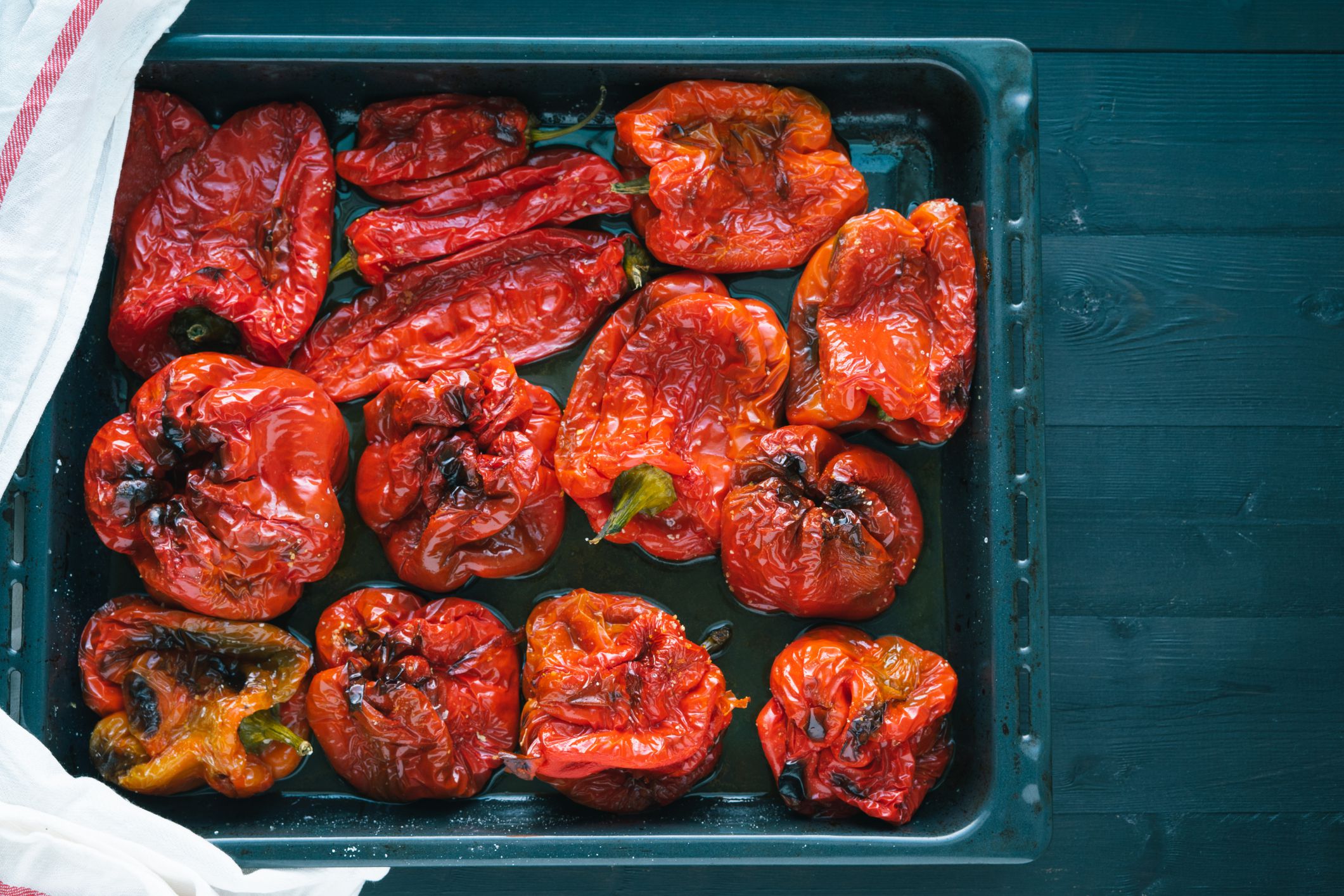 Roasted red peppers in baking tray on black wooden background.