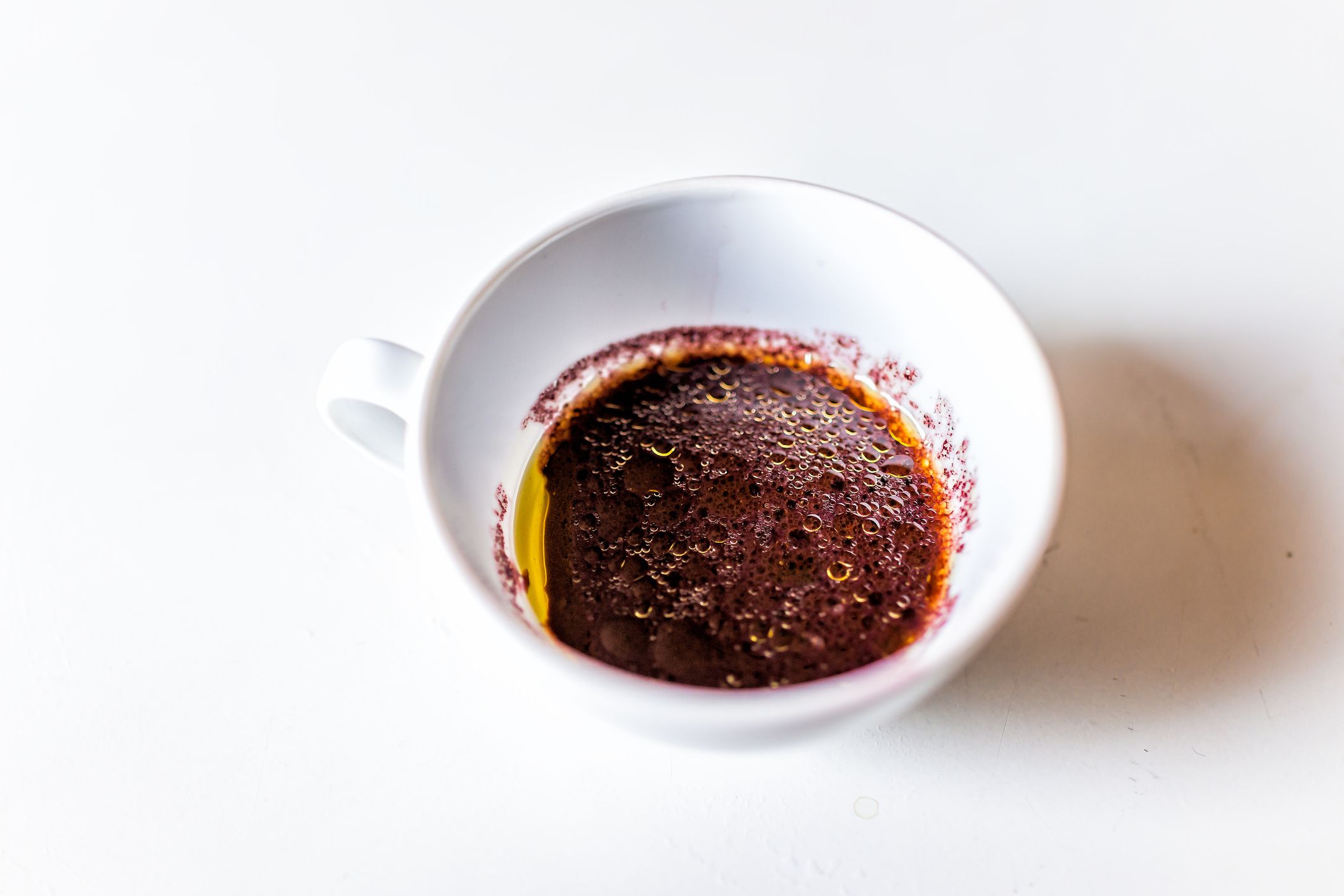 Closeup view above of vibrant red wine sauce in white tea cup in Italian Italy restaurant or kitchen with olive oil isolated background