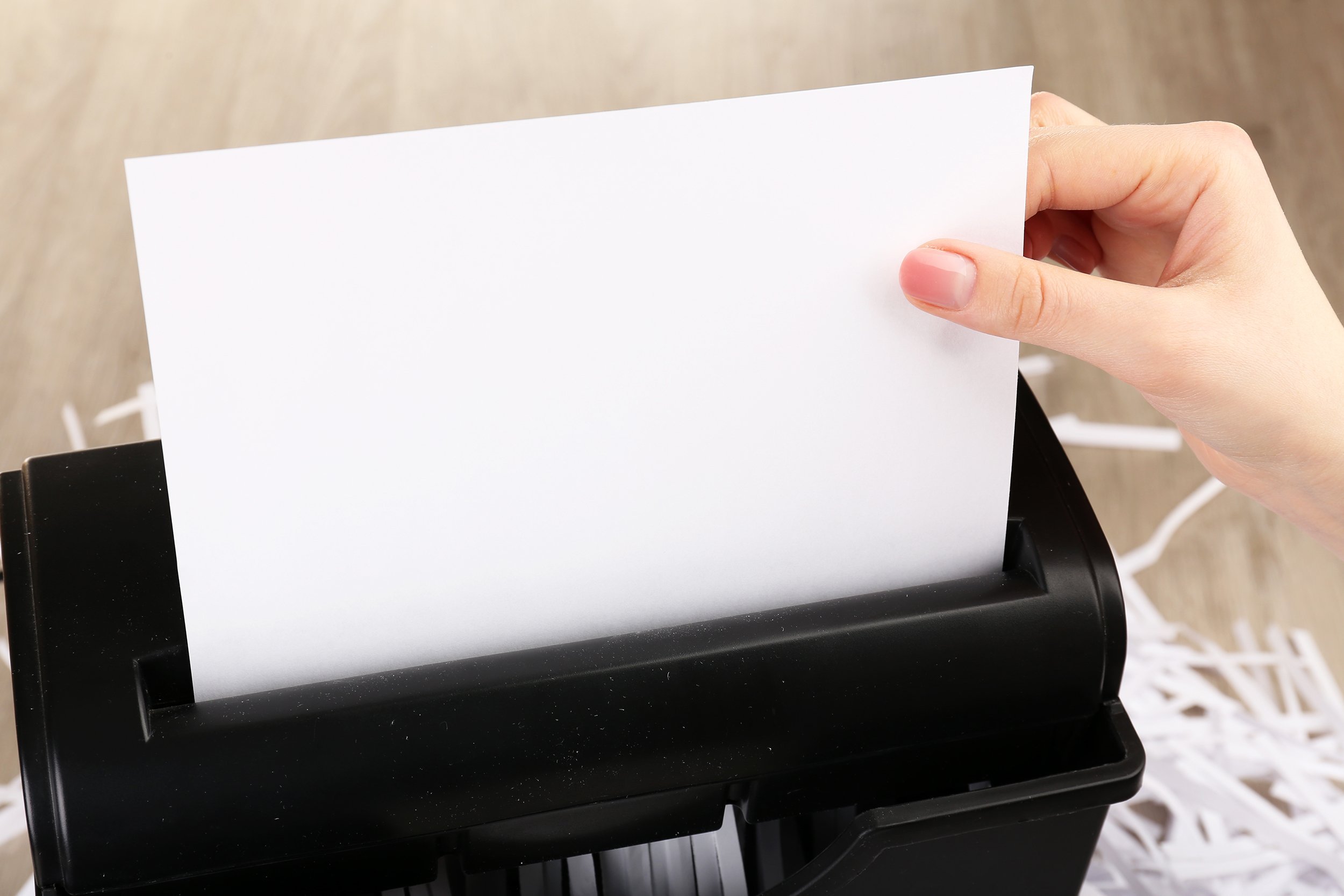 female hand destroying sheet of paper with shredder
