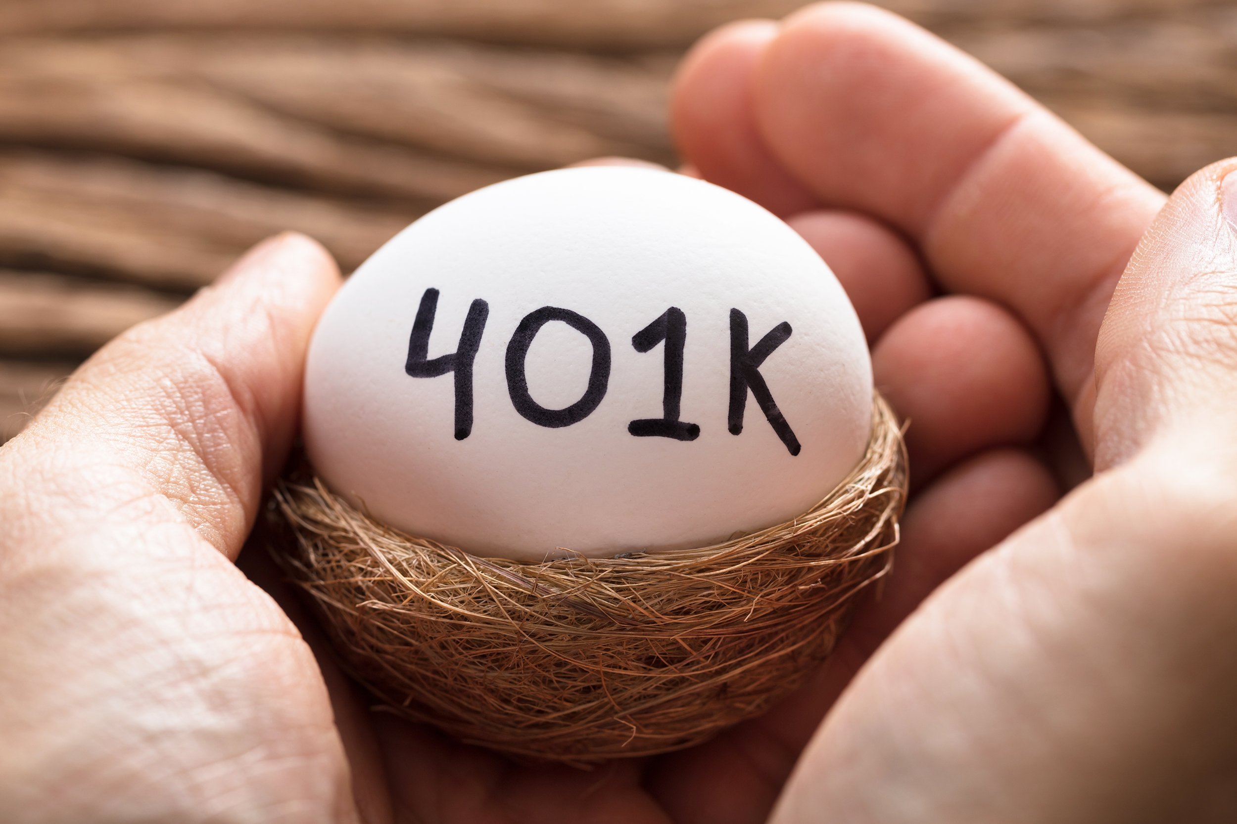 closeup of hands holding 401K white egg in nest