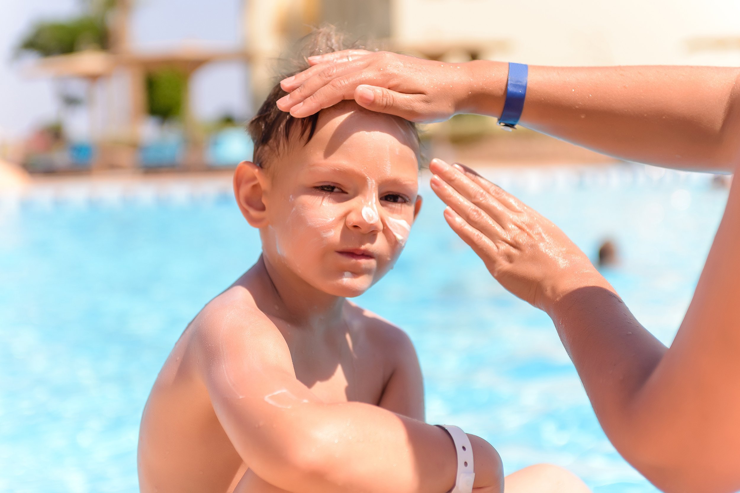 woman applying sunscreen to the face of her young son near the pool