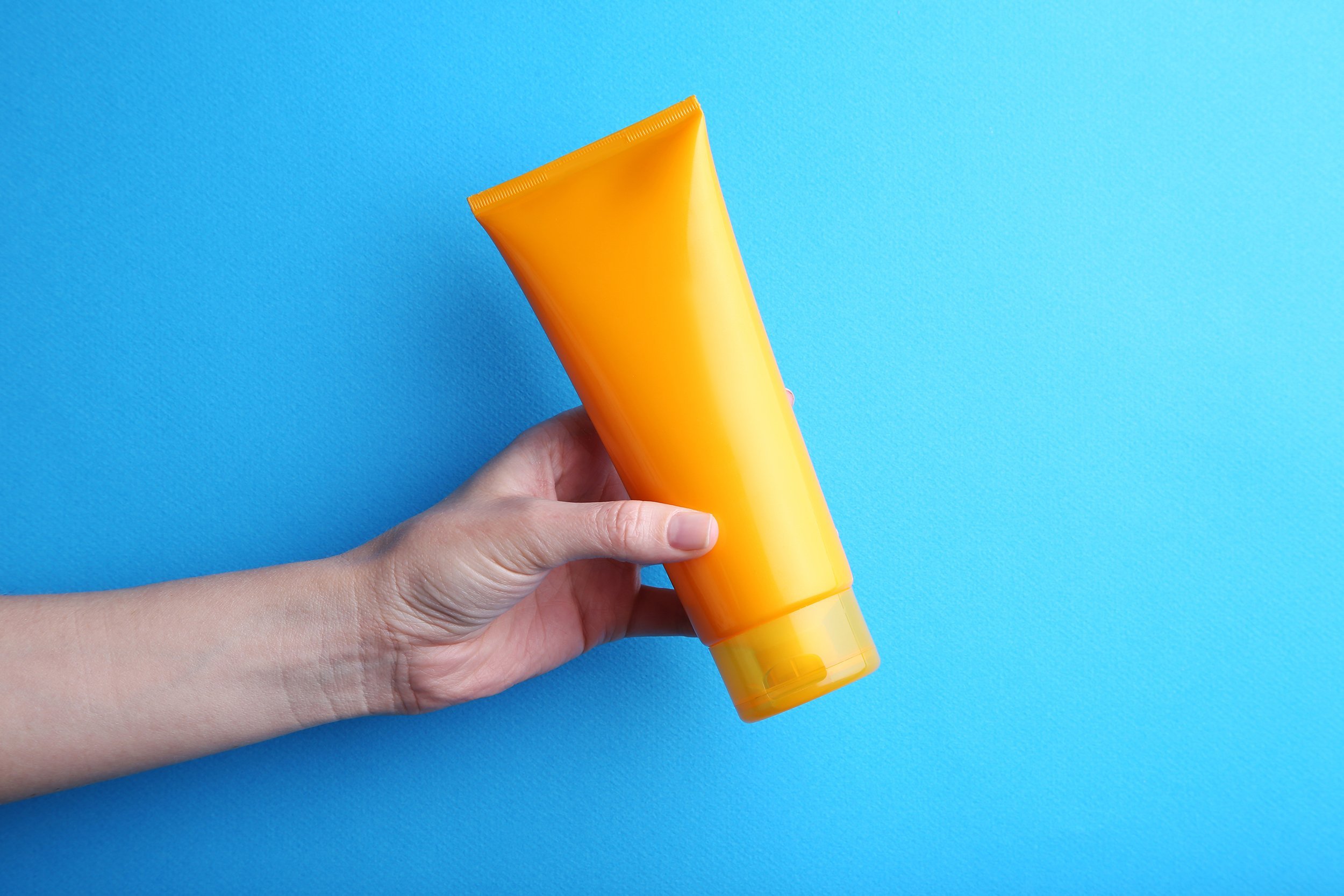 female hand holding sunscreen cream on blue background