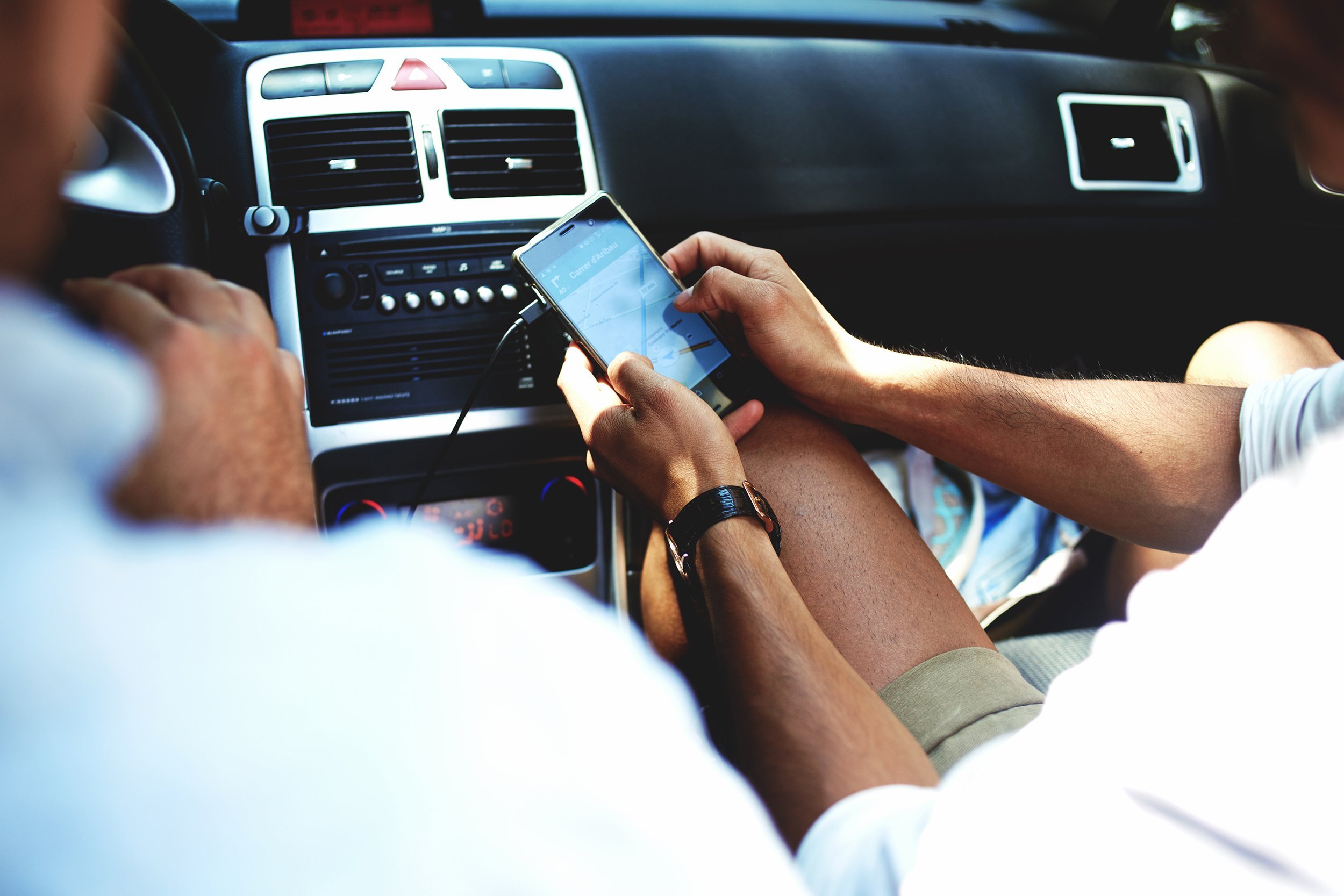 man using navigation on mobile phone while sitting on front passenger seat with driver