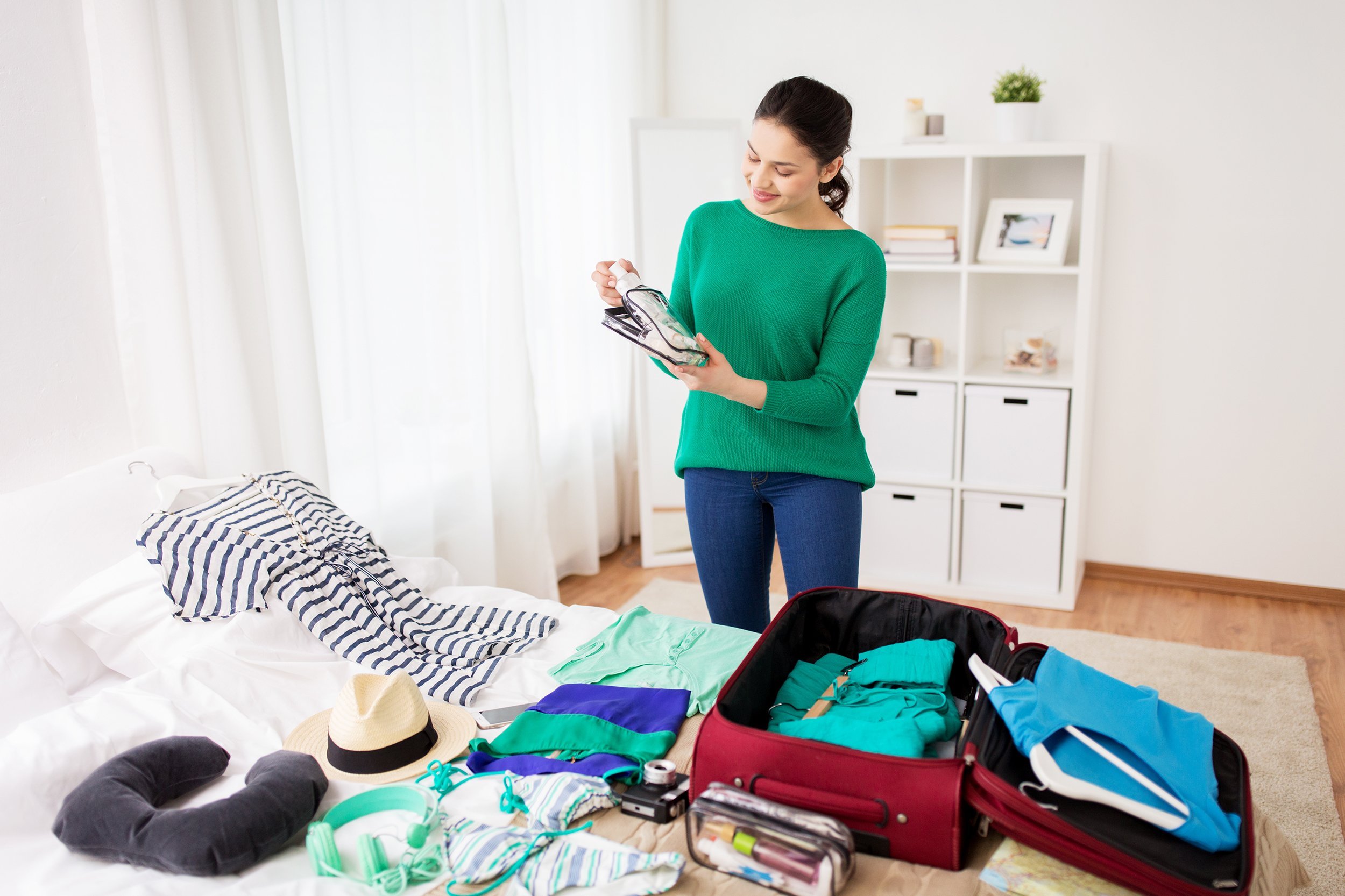 happy young woman packing travel bag at home