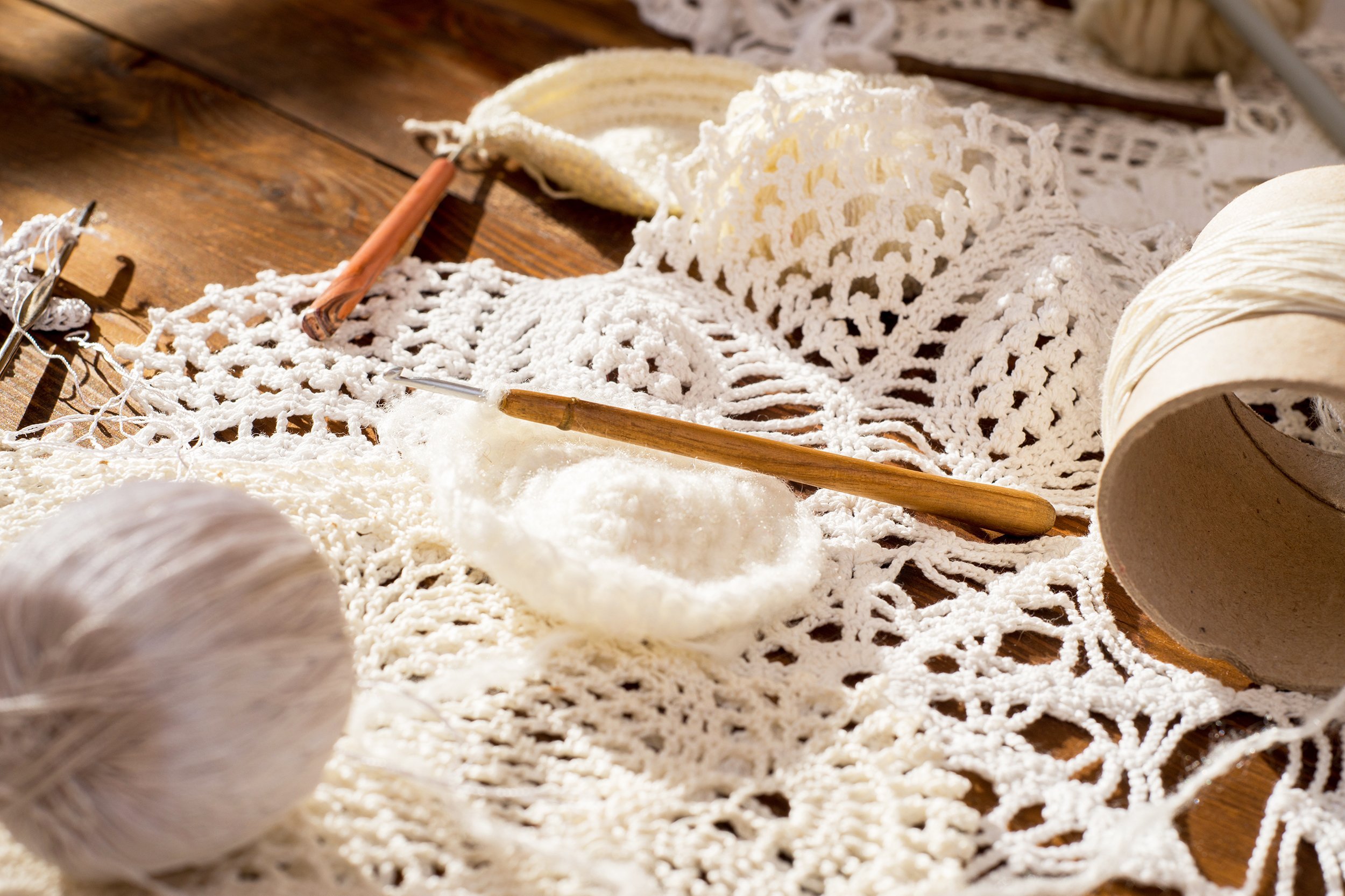 white and beige openwork crochet doily, and balls of wool on a wooden table