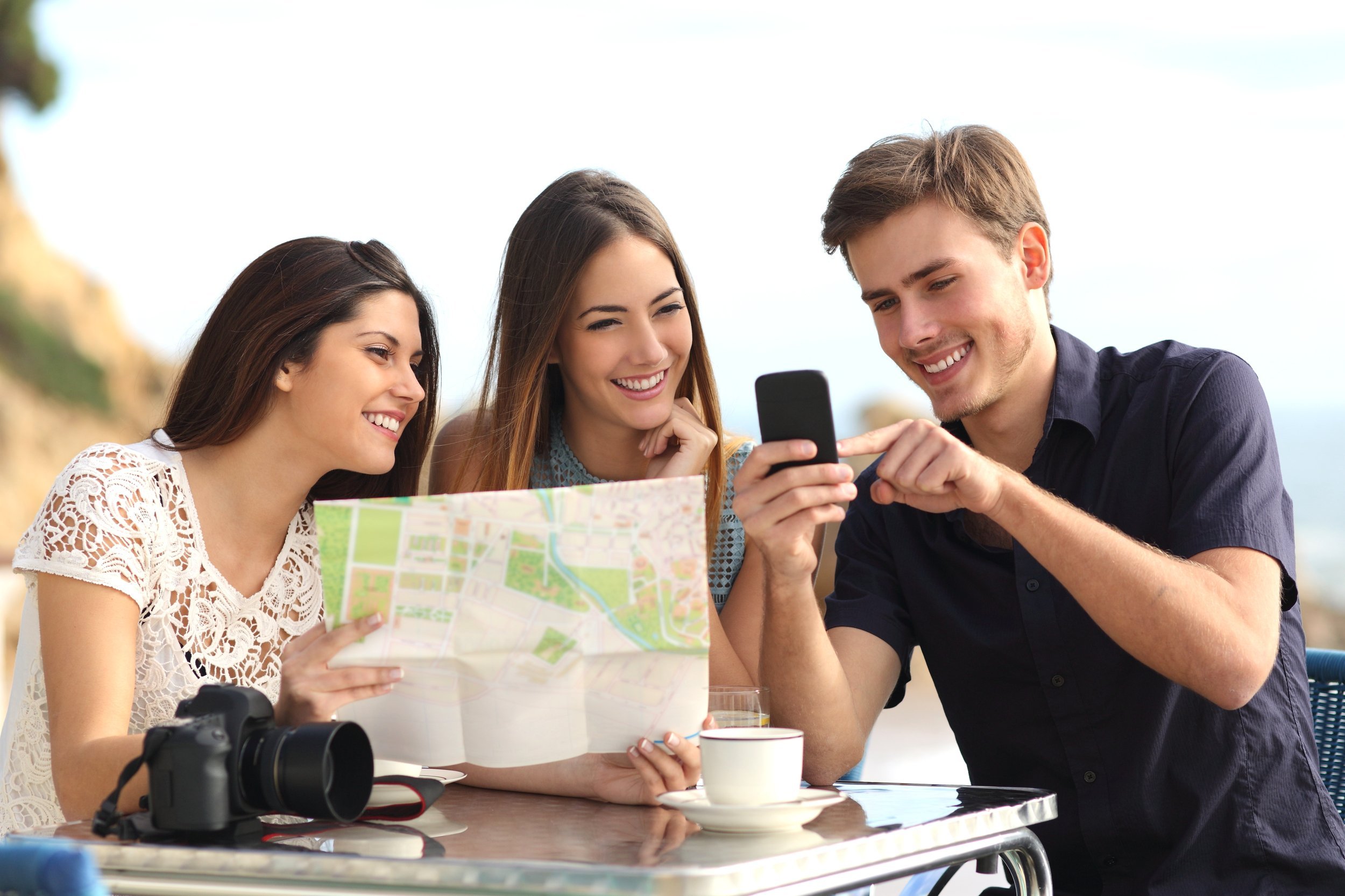 Group of young tourist friends consulting gps map in a smart phone in a restaurant with the beach in the background.