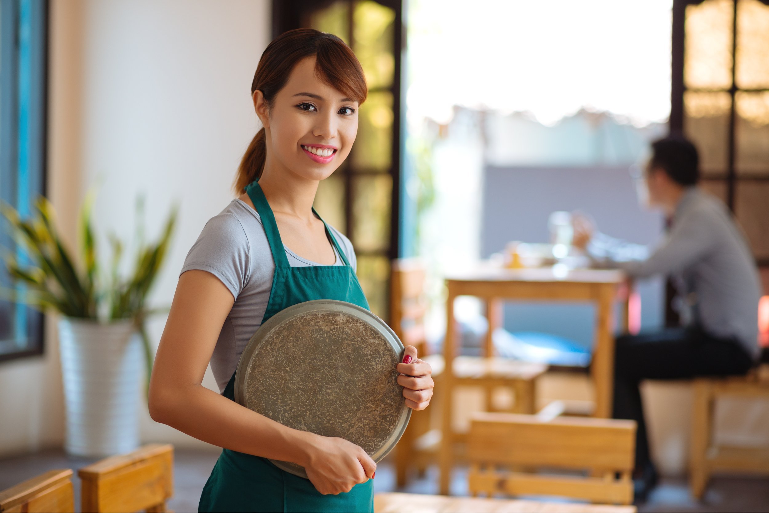 Portrait of Vietnamese beautiful waitress with a tray standing in a cafe.