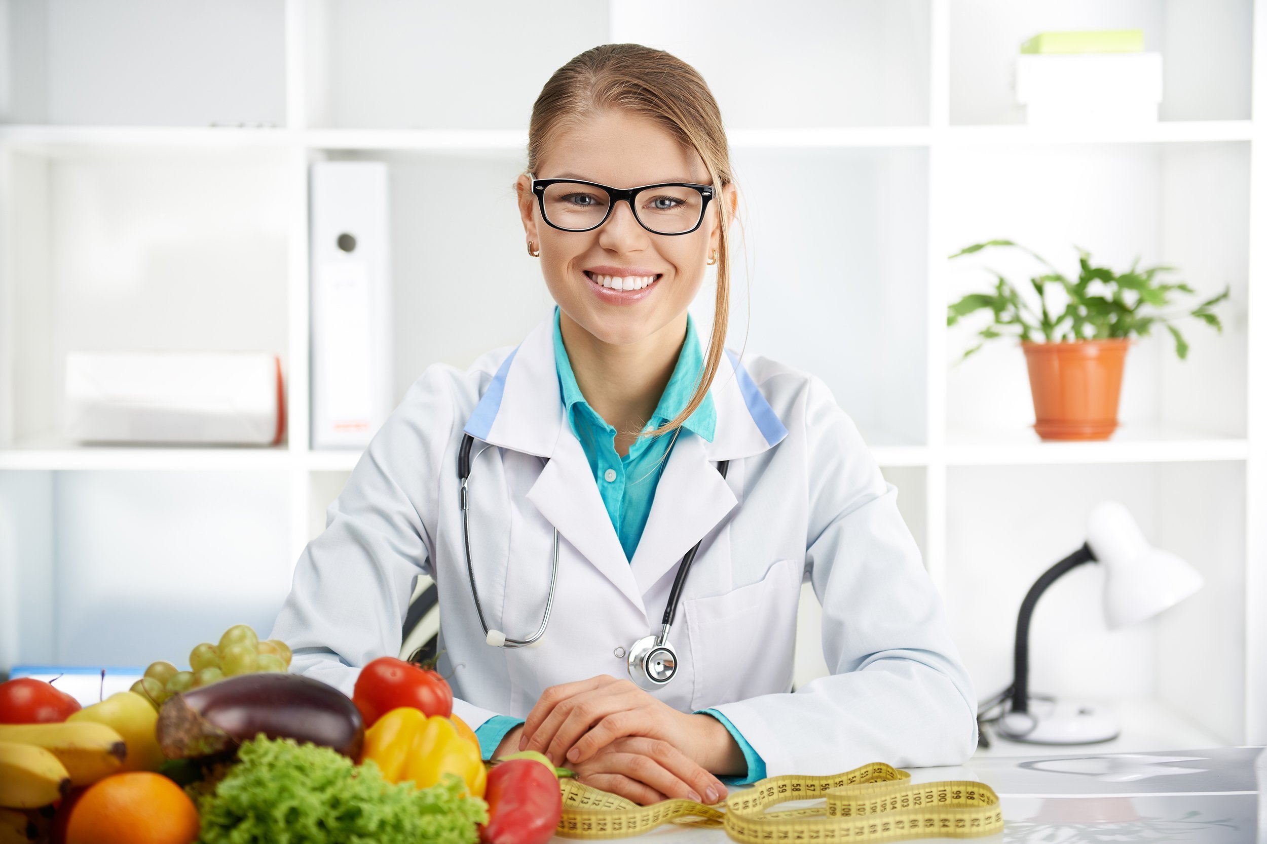 smiling female dietitian sitting at the table with colorful fruits and vegetables in clinic