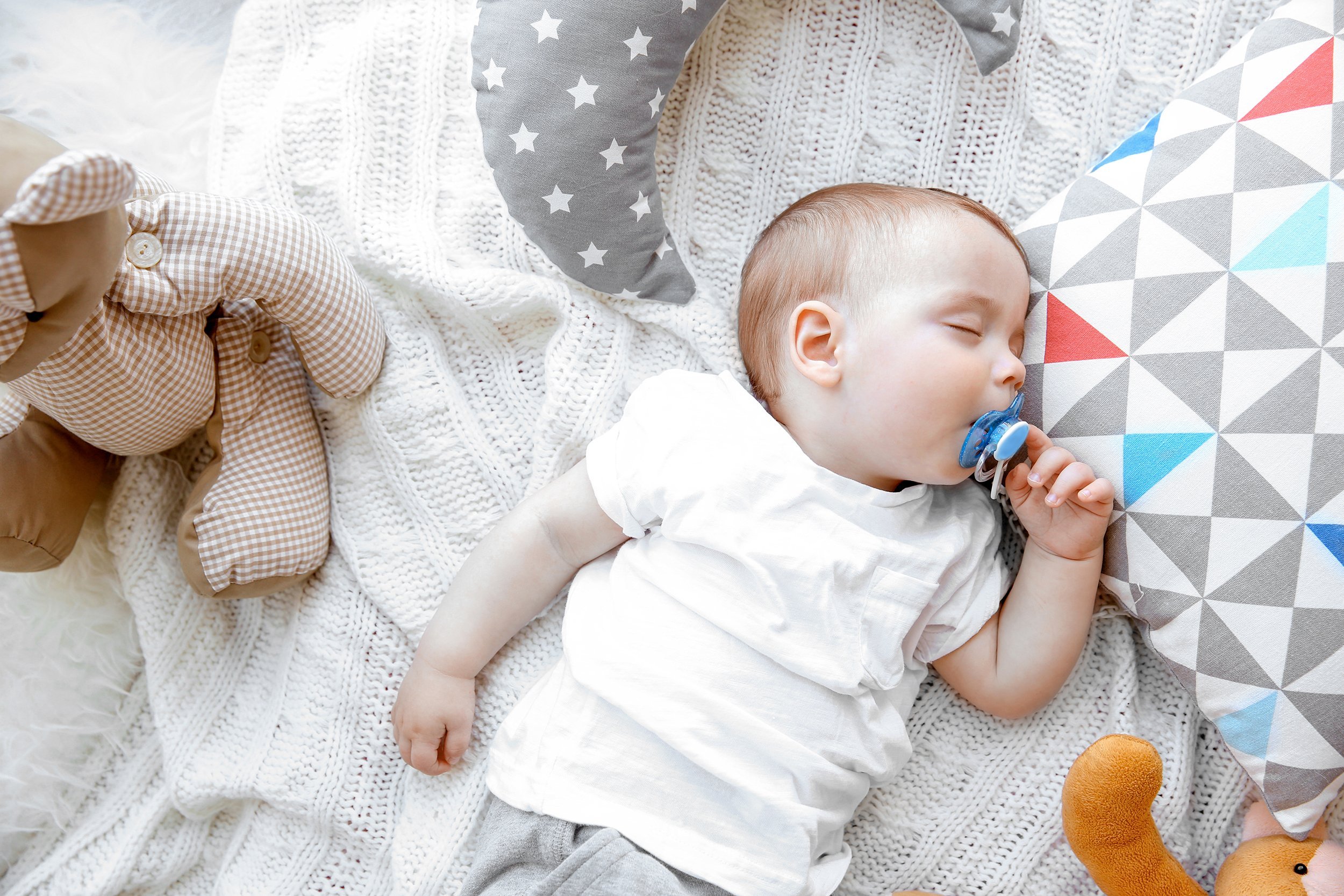 Sleeping baby boy surrounded by toys and pillows