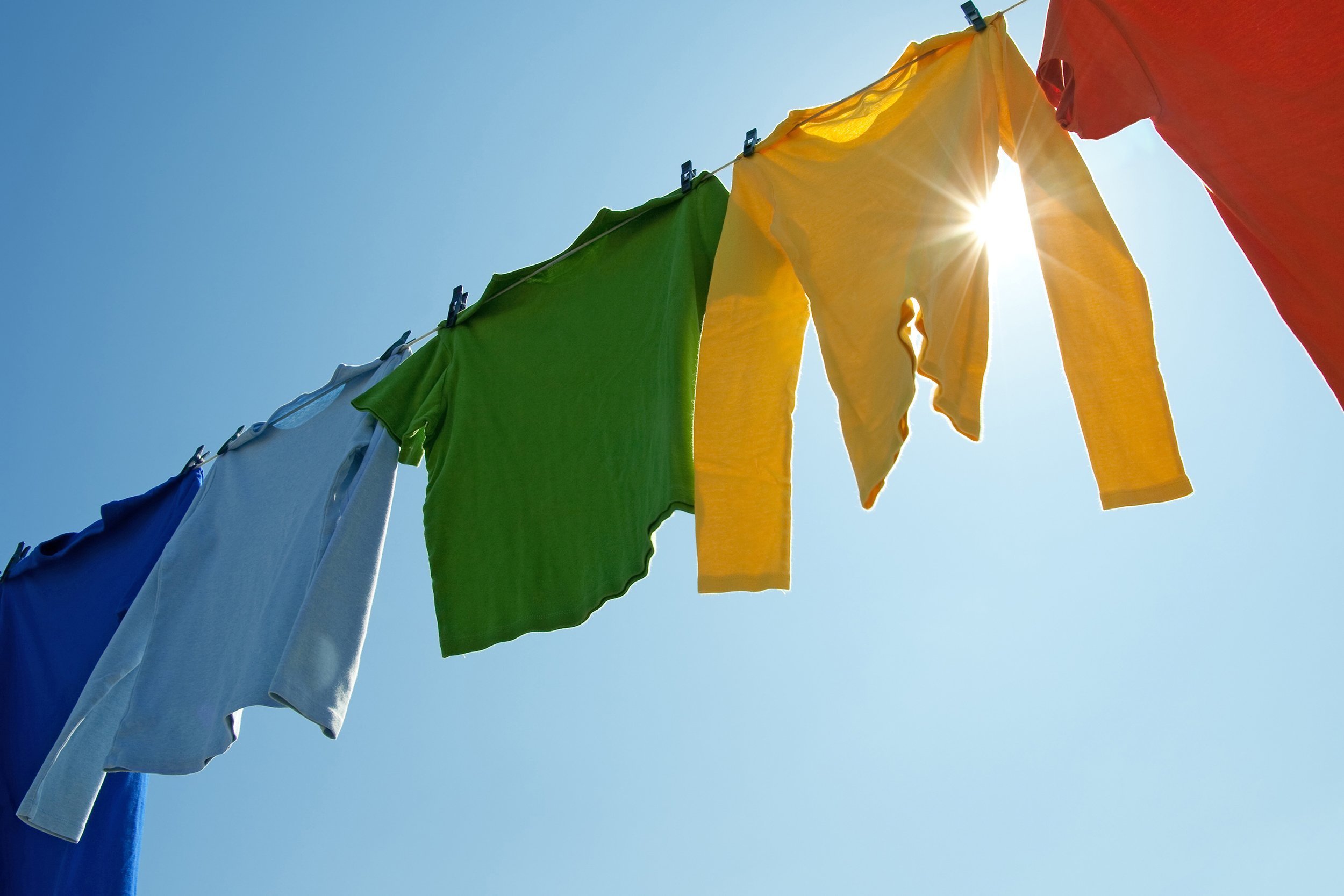 colorful shirts hanging to dry on a laundry line and sun shining in the blue sky
