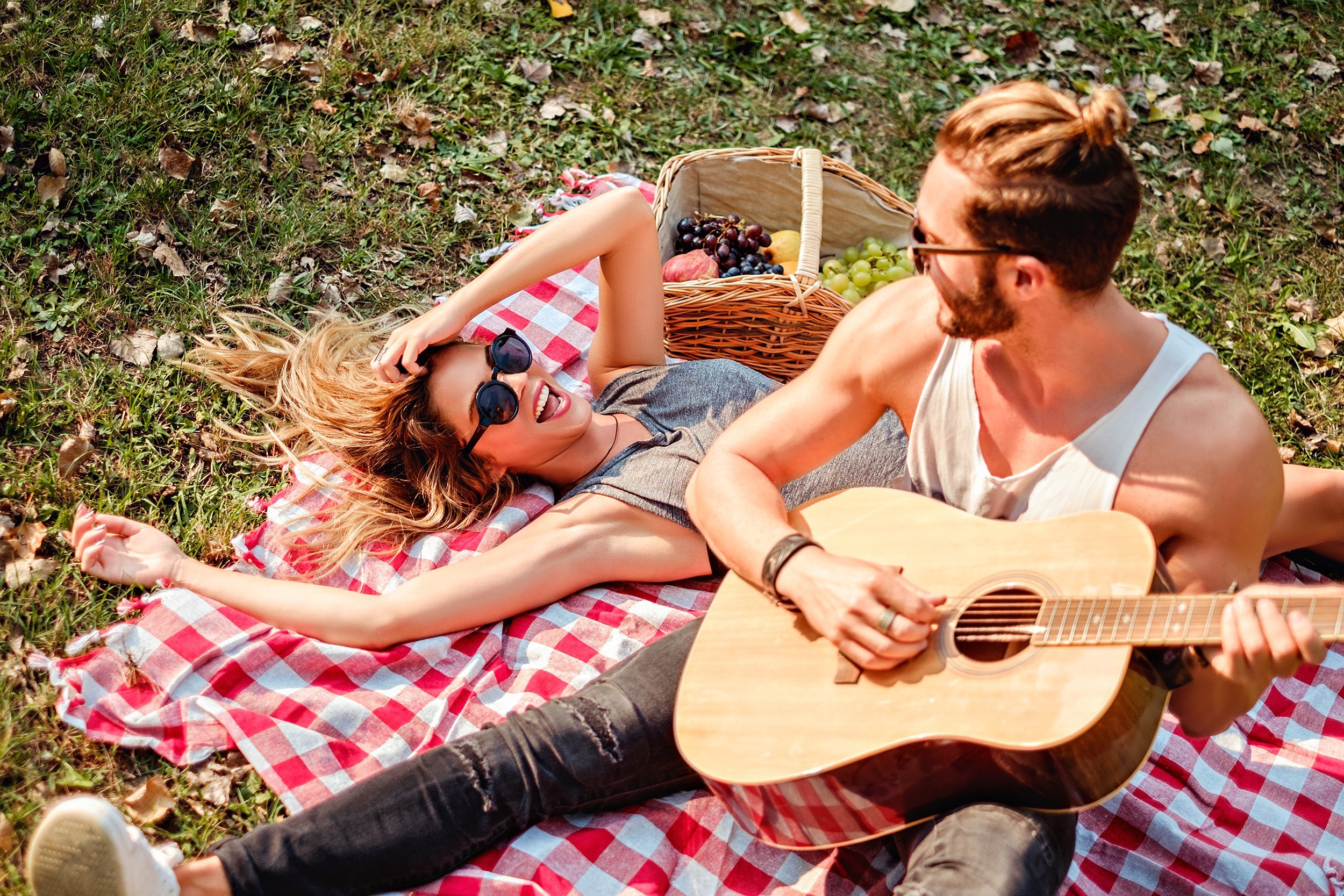 man playing guitar to his girl on a picnic