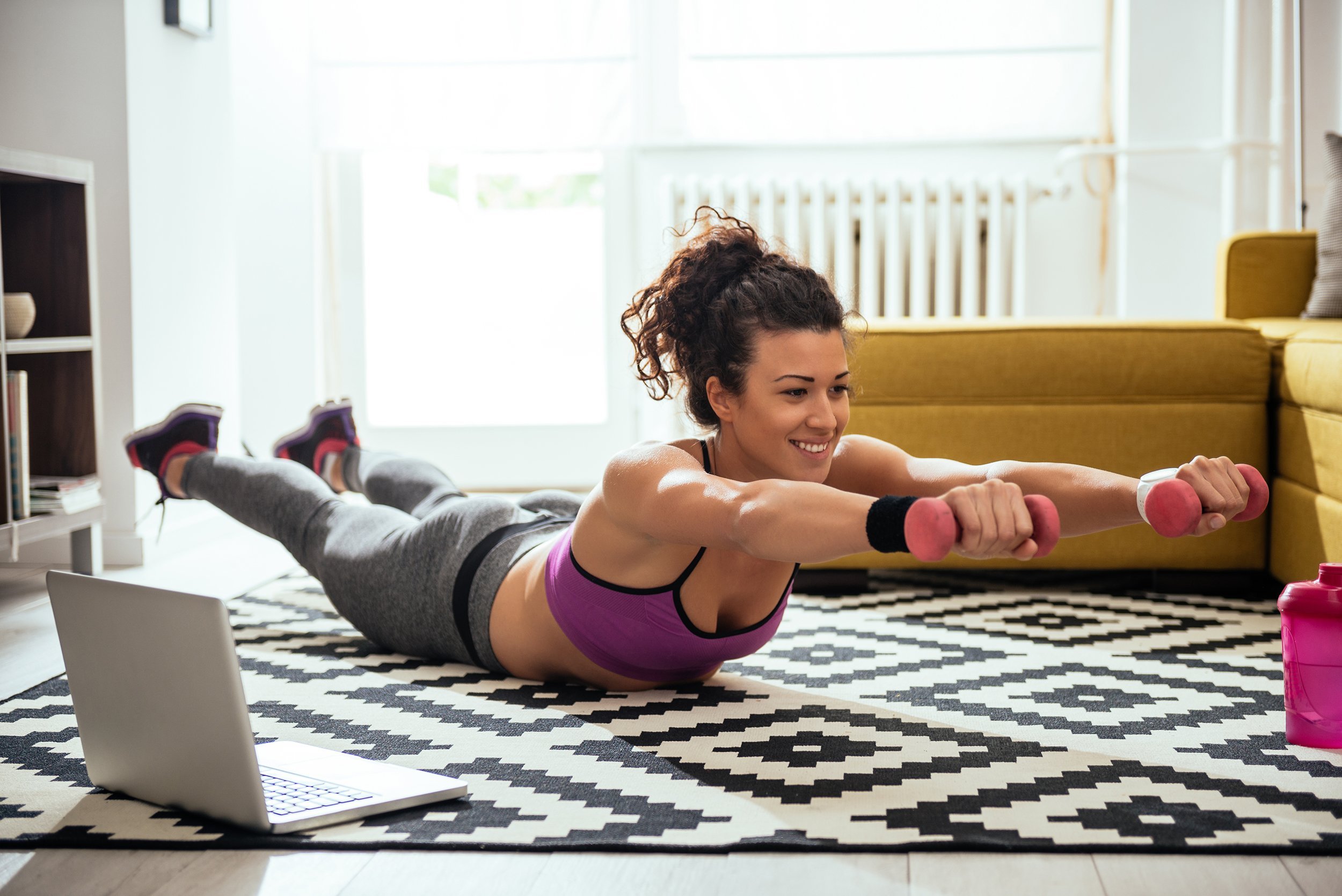 young woman exercising at home in a living room in front of laptop