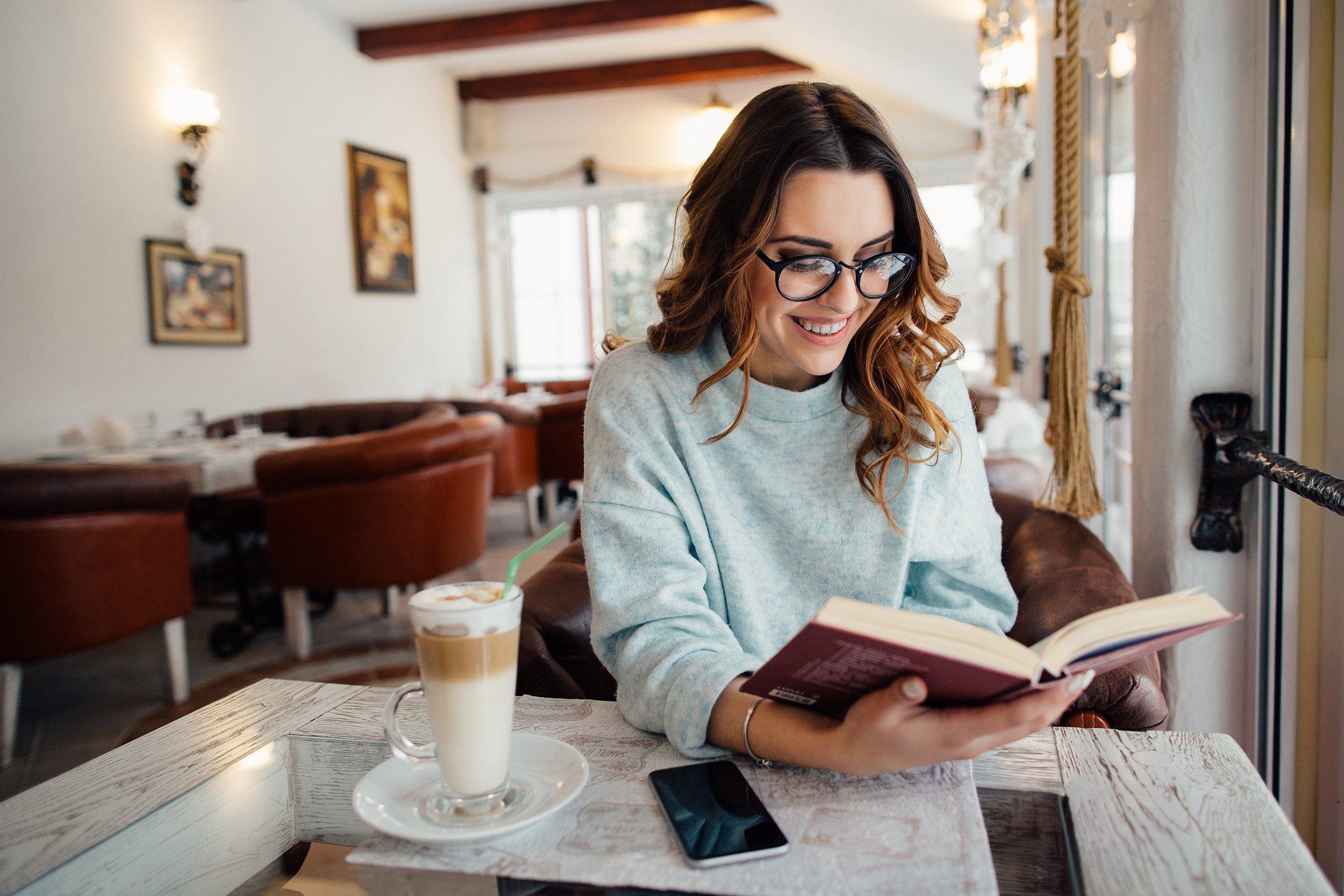 woman in glasses reading interesting book in cafe