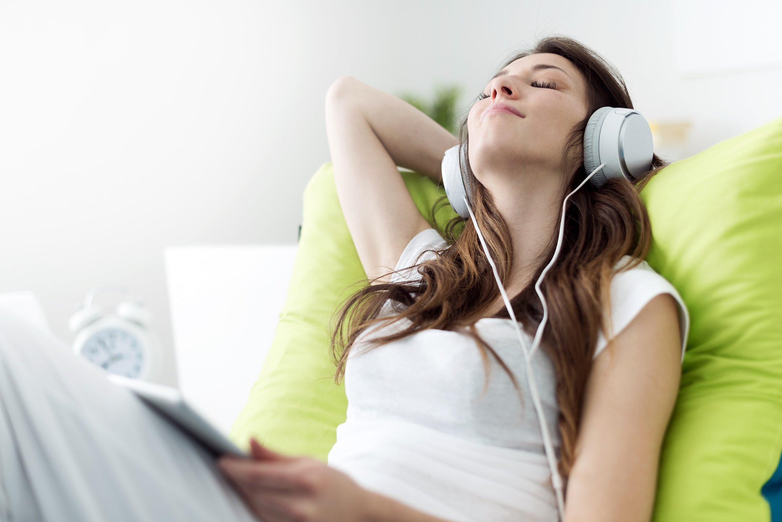 woman with headphones relaxing on the bed listening to music using a tablet