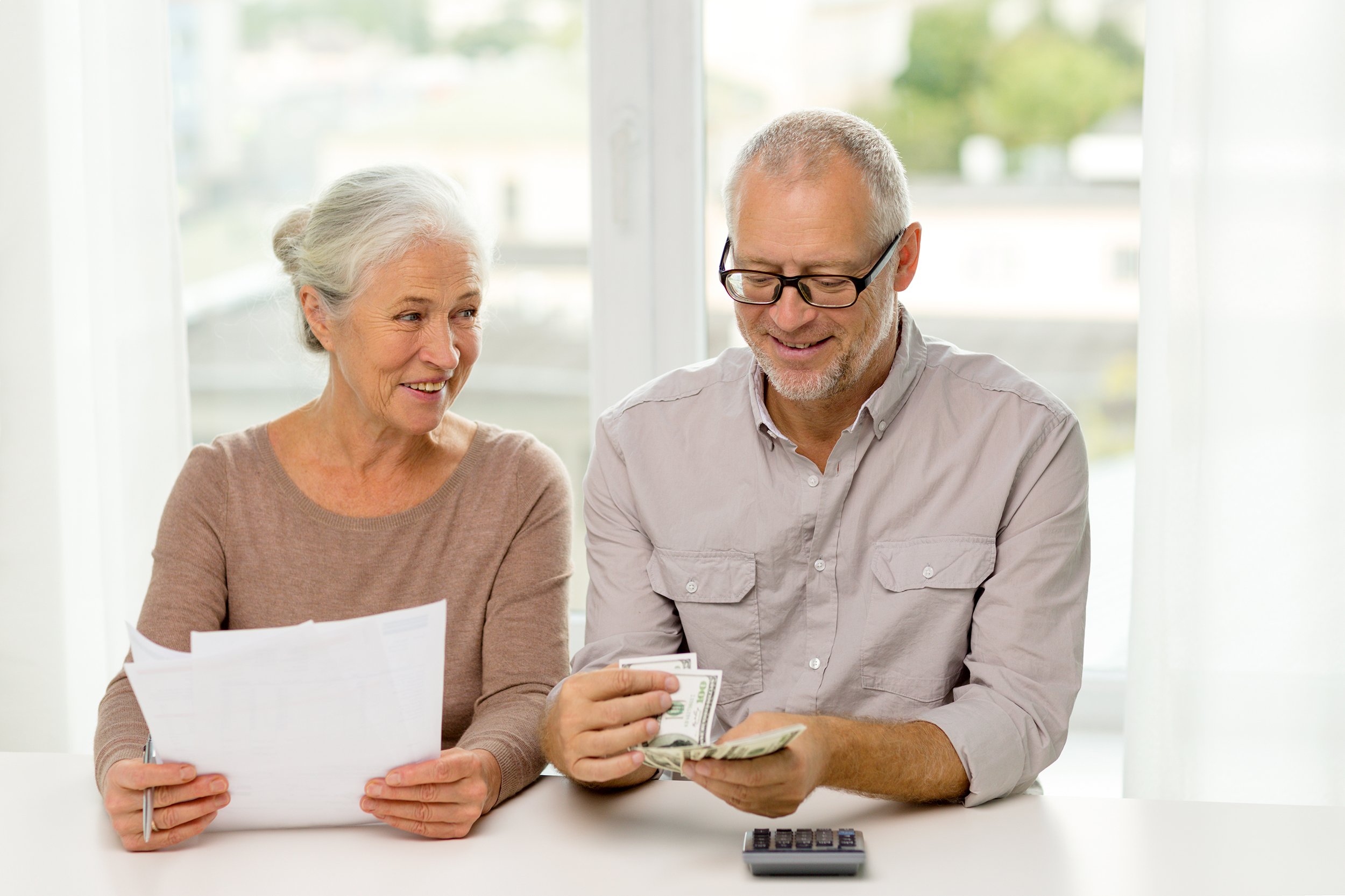Smiling senior couple with papers, money, and a calculator at home