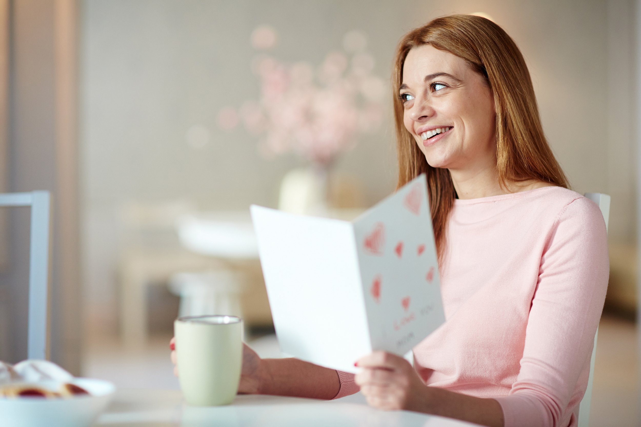 young woman with cup of drink reading greeting card