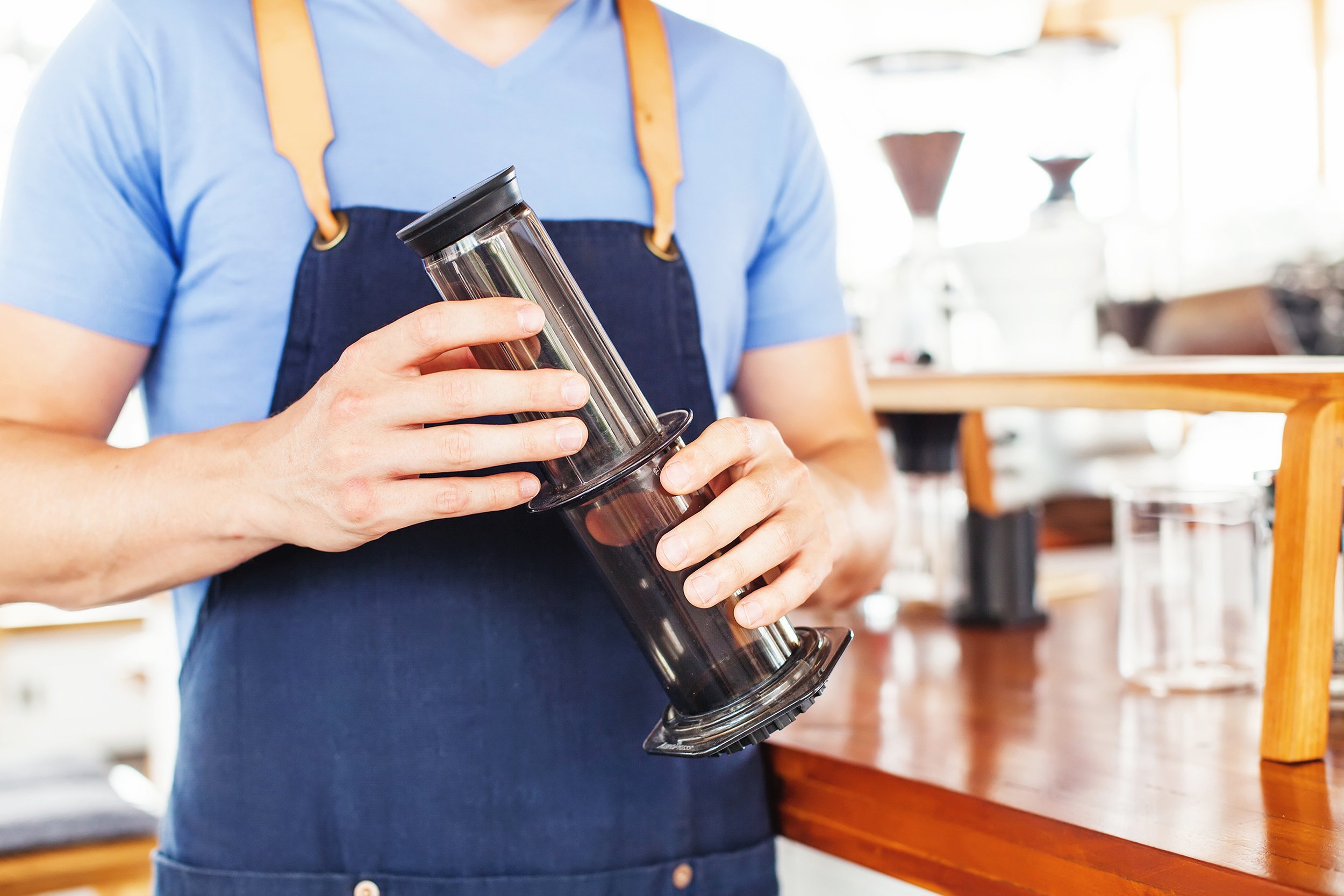 man in coffee shop holding aeropress