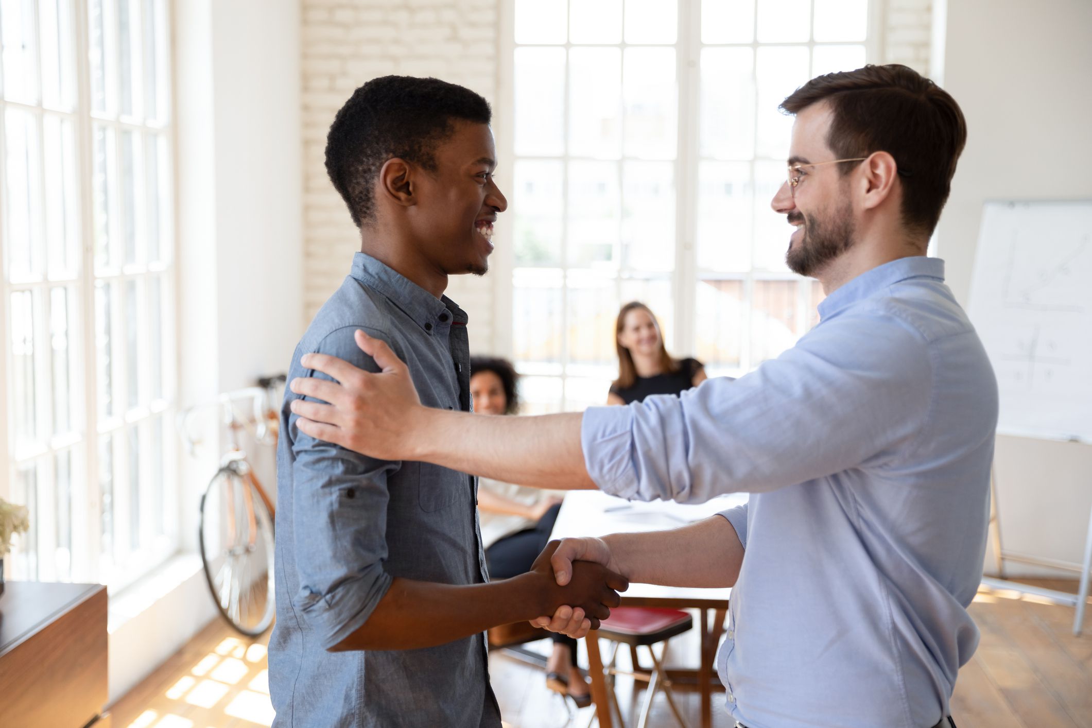 Smiling young male boss shaking hands with african employee.