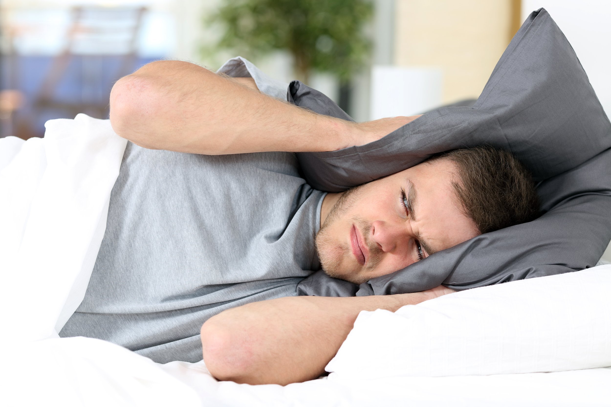 Man trying to sleep covering head with pillow to avoid noise