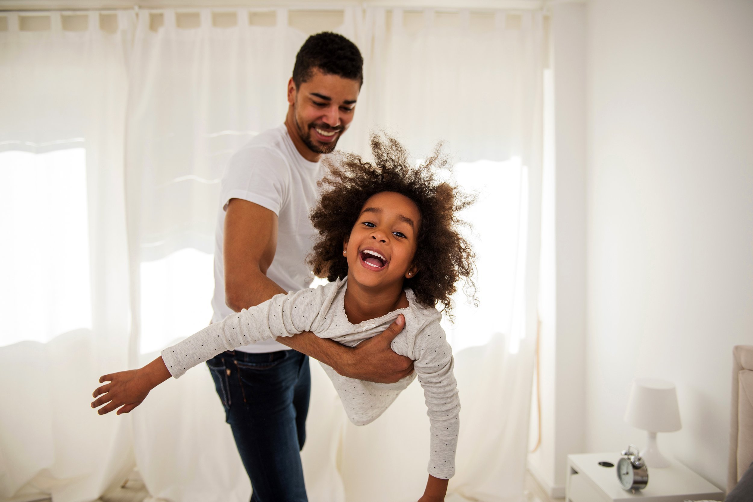 African American man playing with his child on a hotel bed