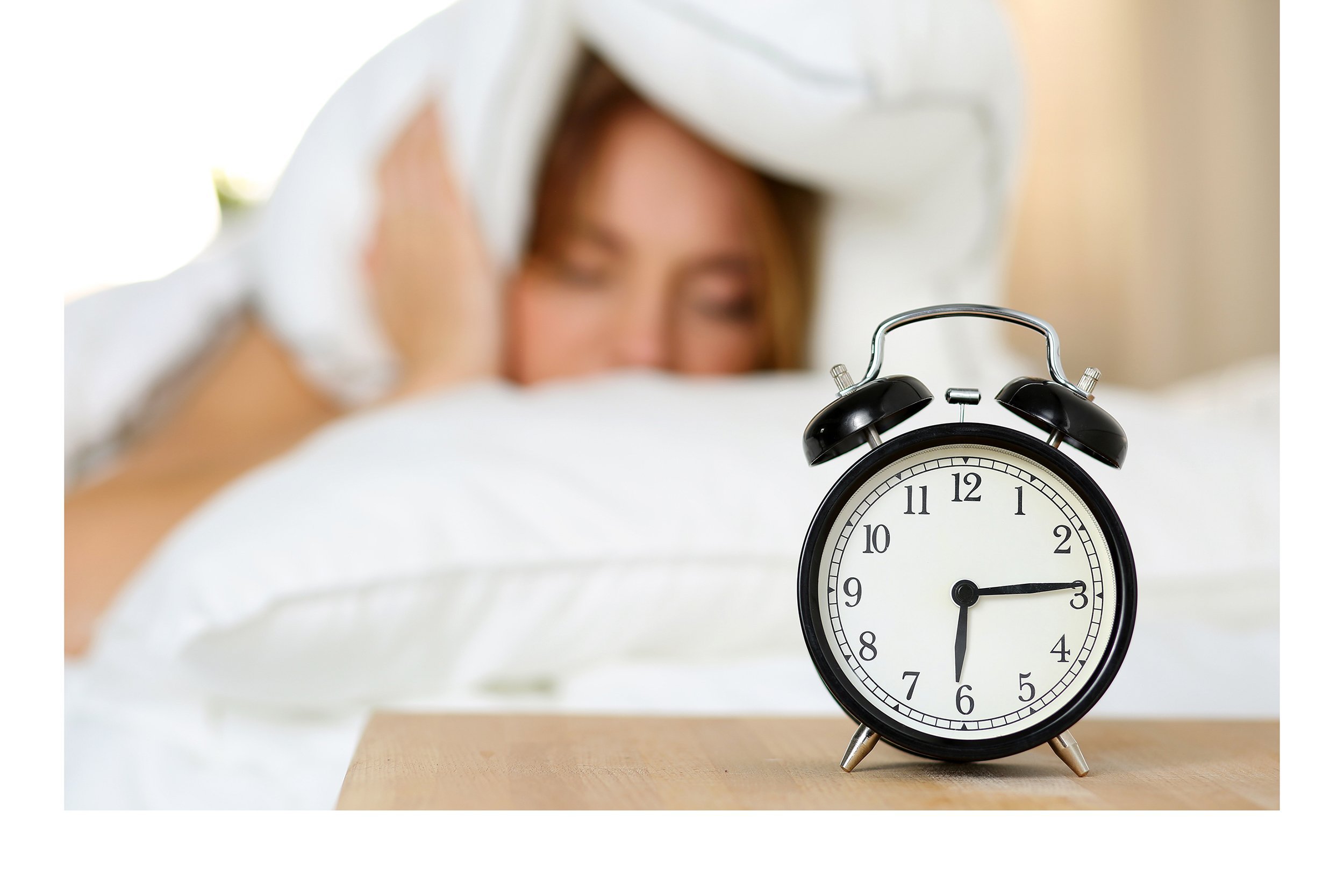 Woman wanting to sleep in and alarm clock showing early time