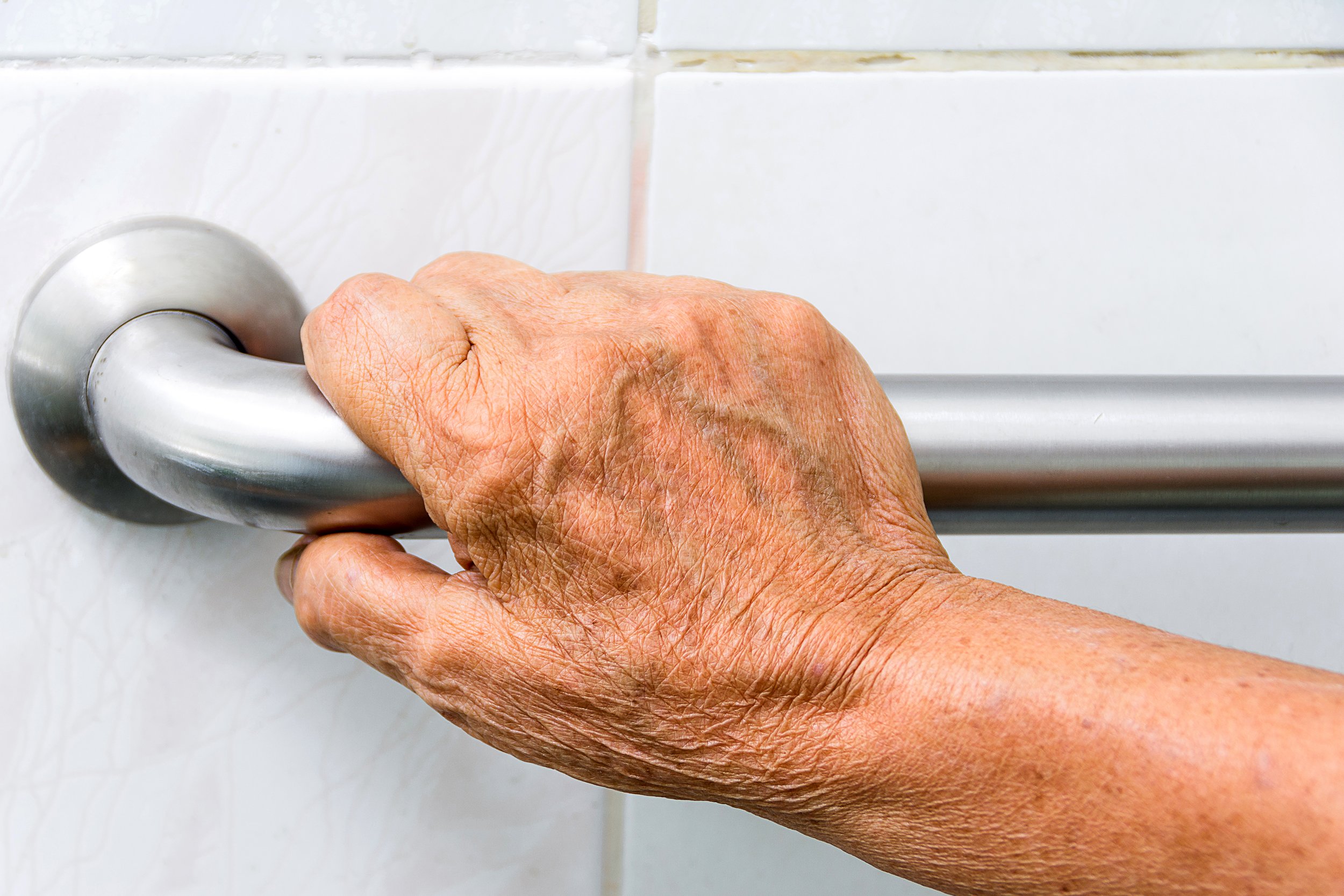 Close-up of elderly hand using a grab bar in a bathroom