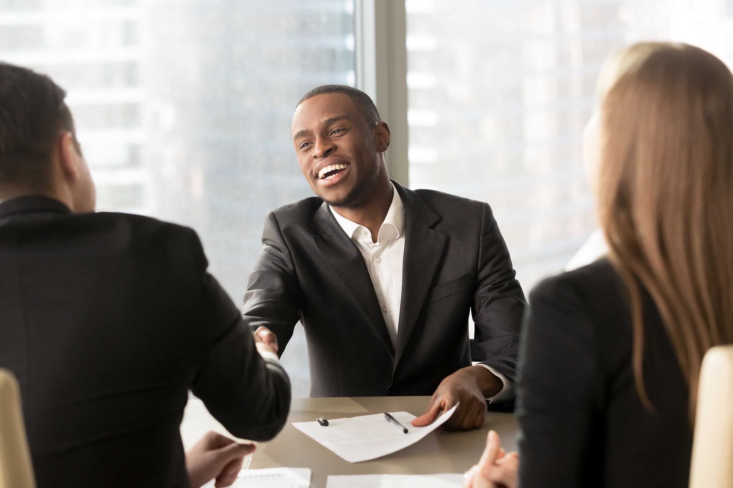 Cheerful employee or boss sitting across from two people at an office desk