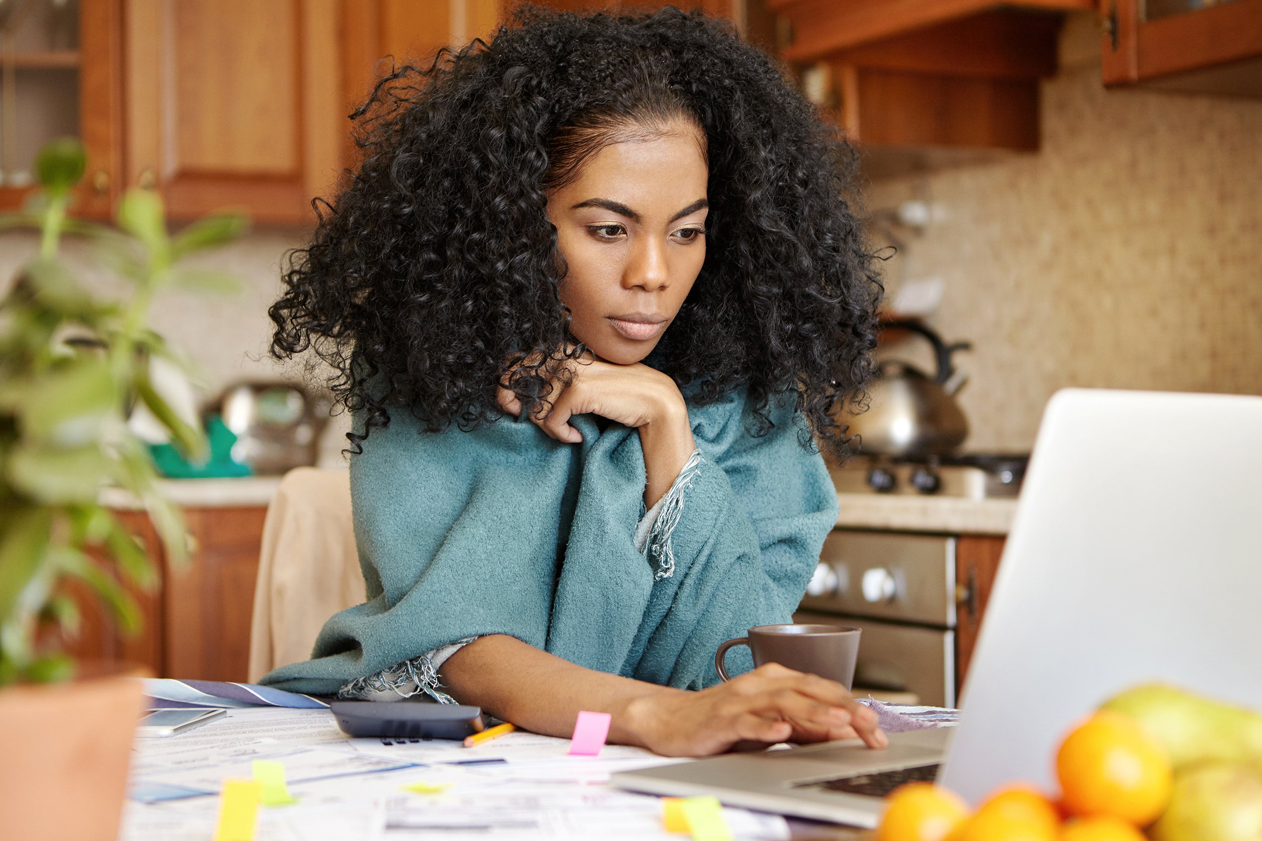 Young African American woman sitting at kitchen table looking concerned at laptop