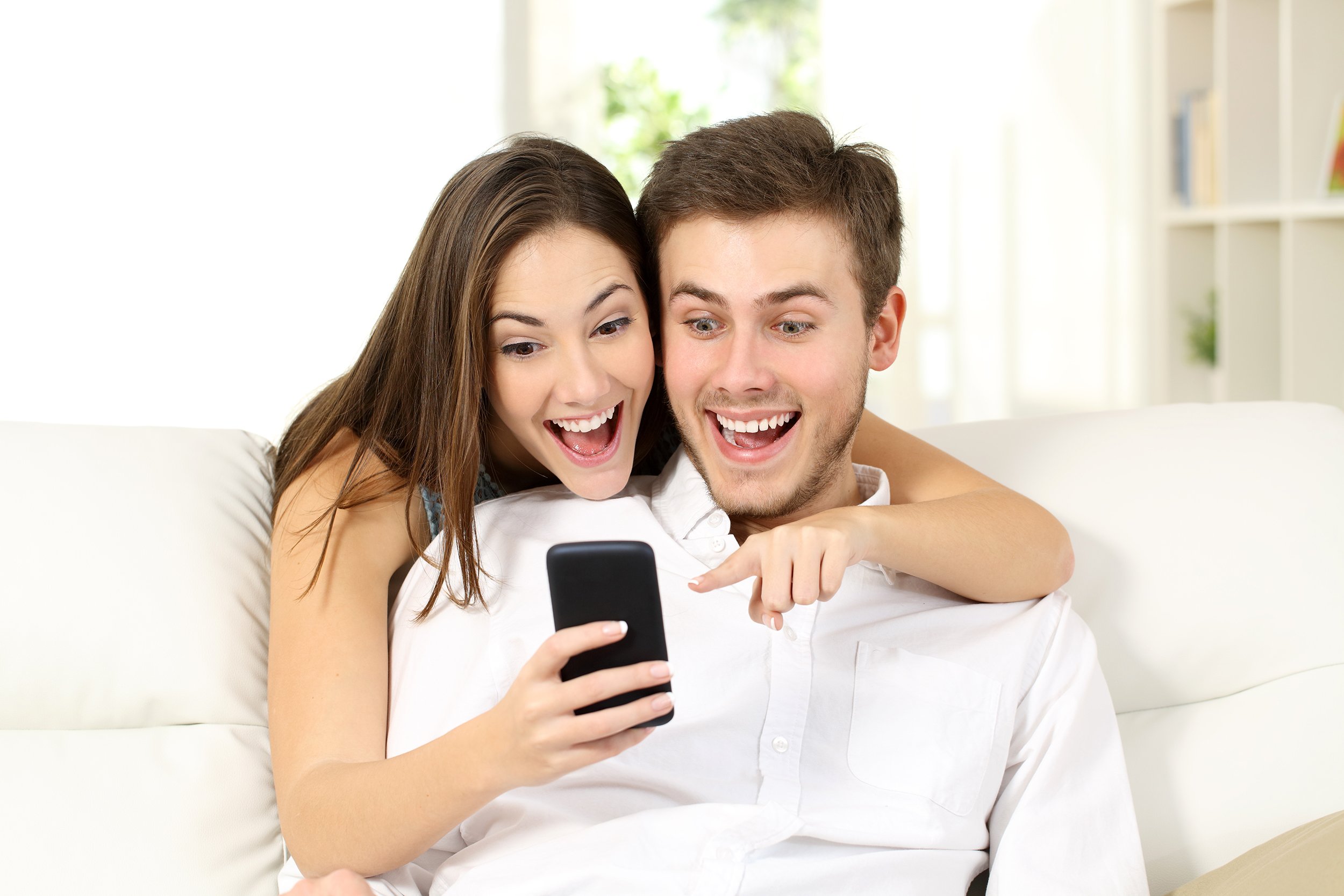 Happy and surprised looking couple at home looking at smart phone