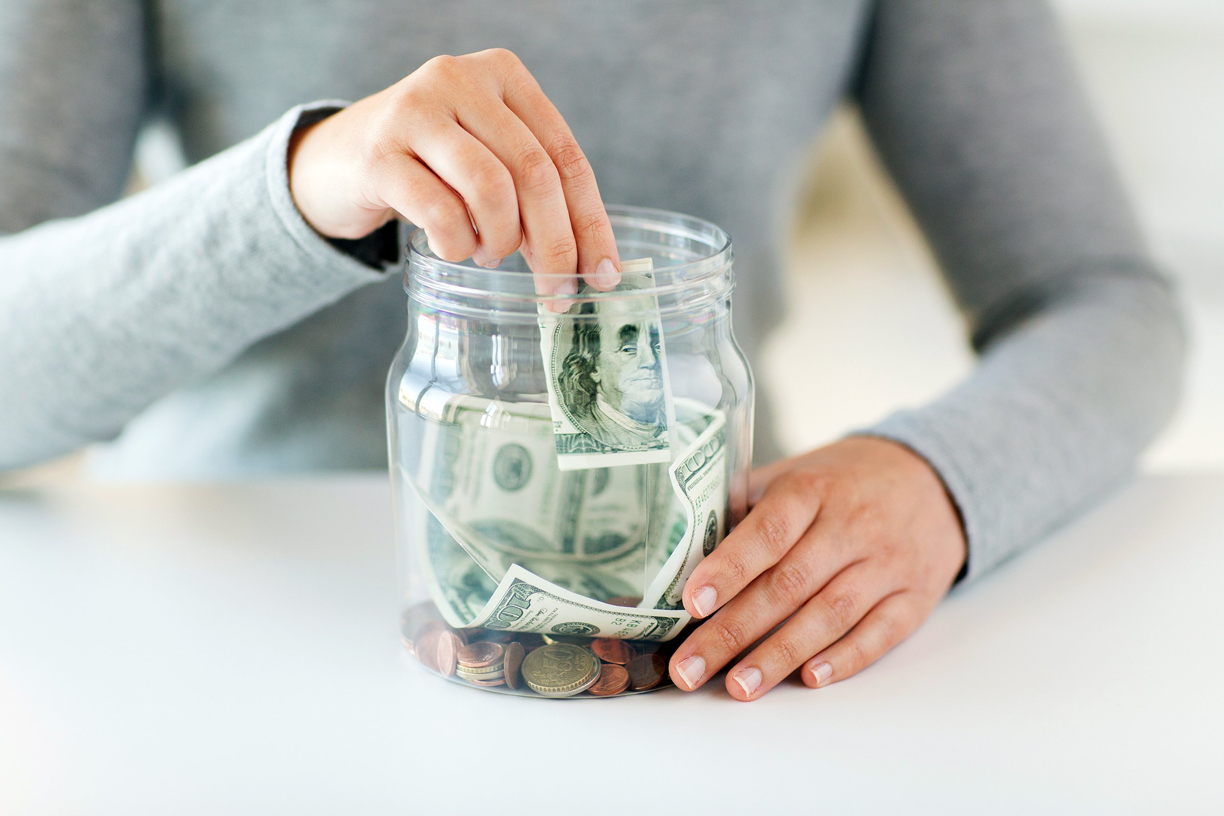 close up of woman hands putting us dollar money into glass mason jar