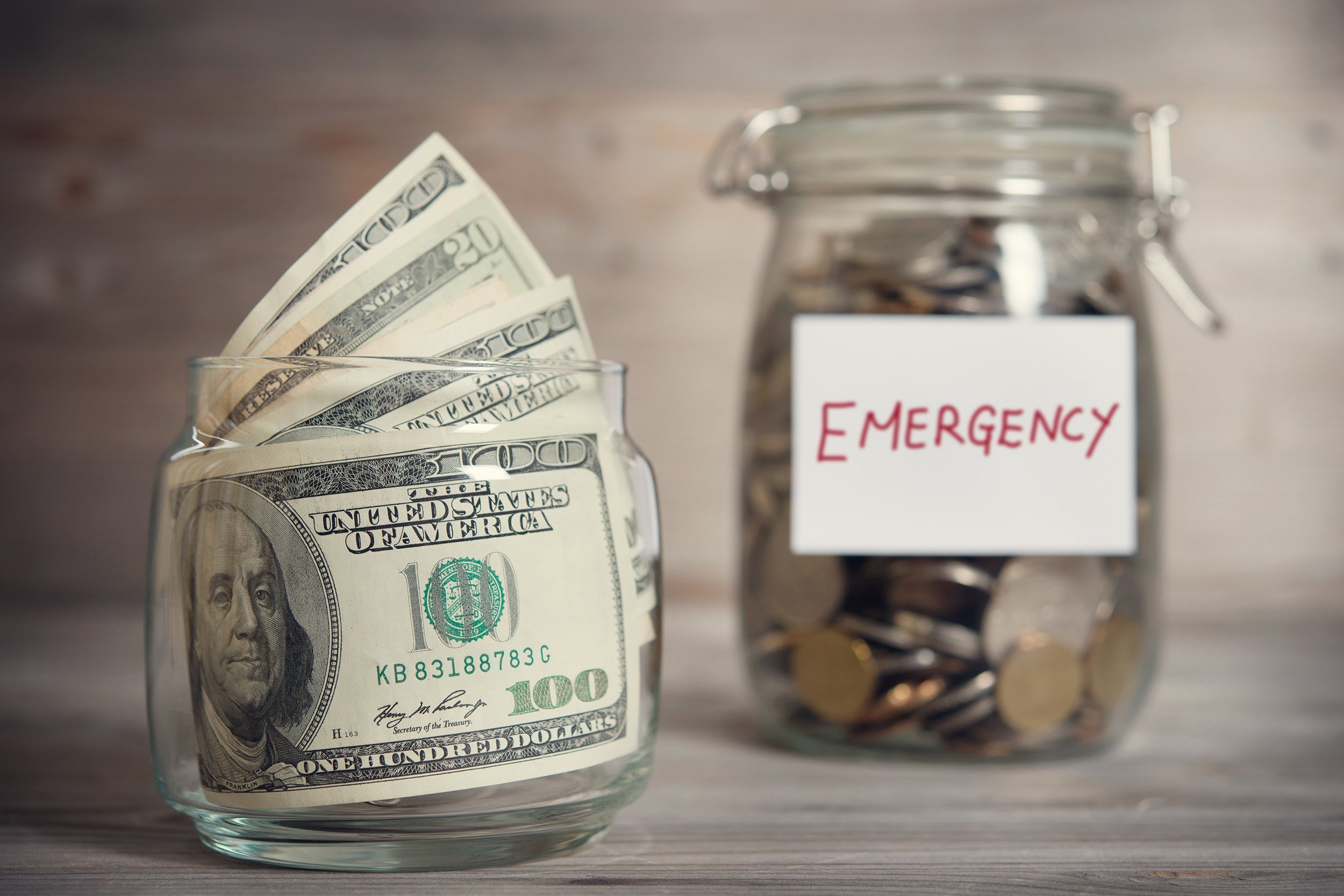 coins and money in glass jar with emergency label on wooden background