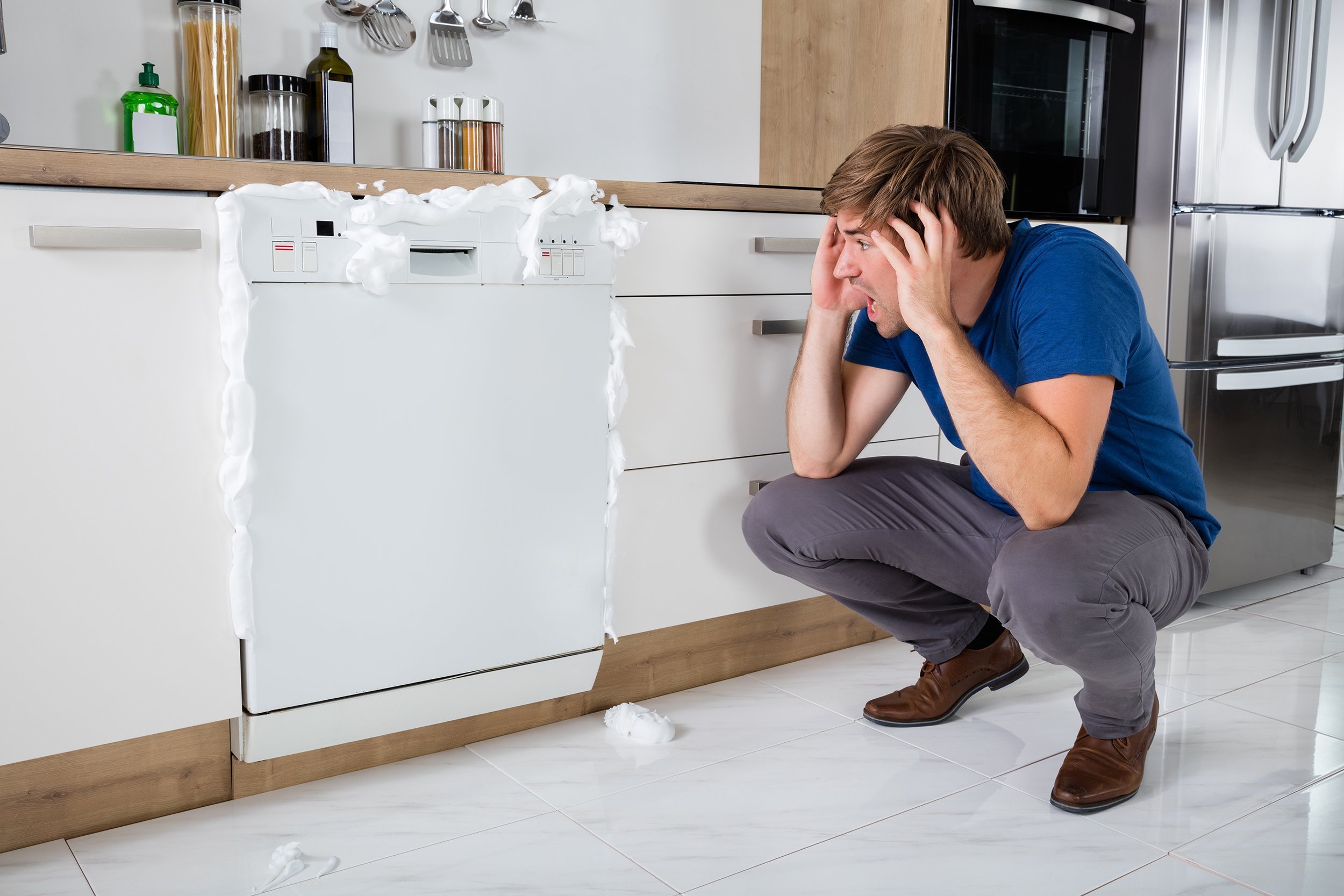 young man shocked on seeing foam coming out of dishwasher at home