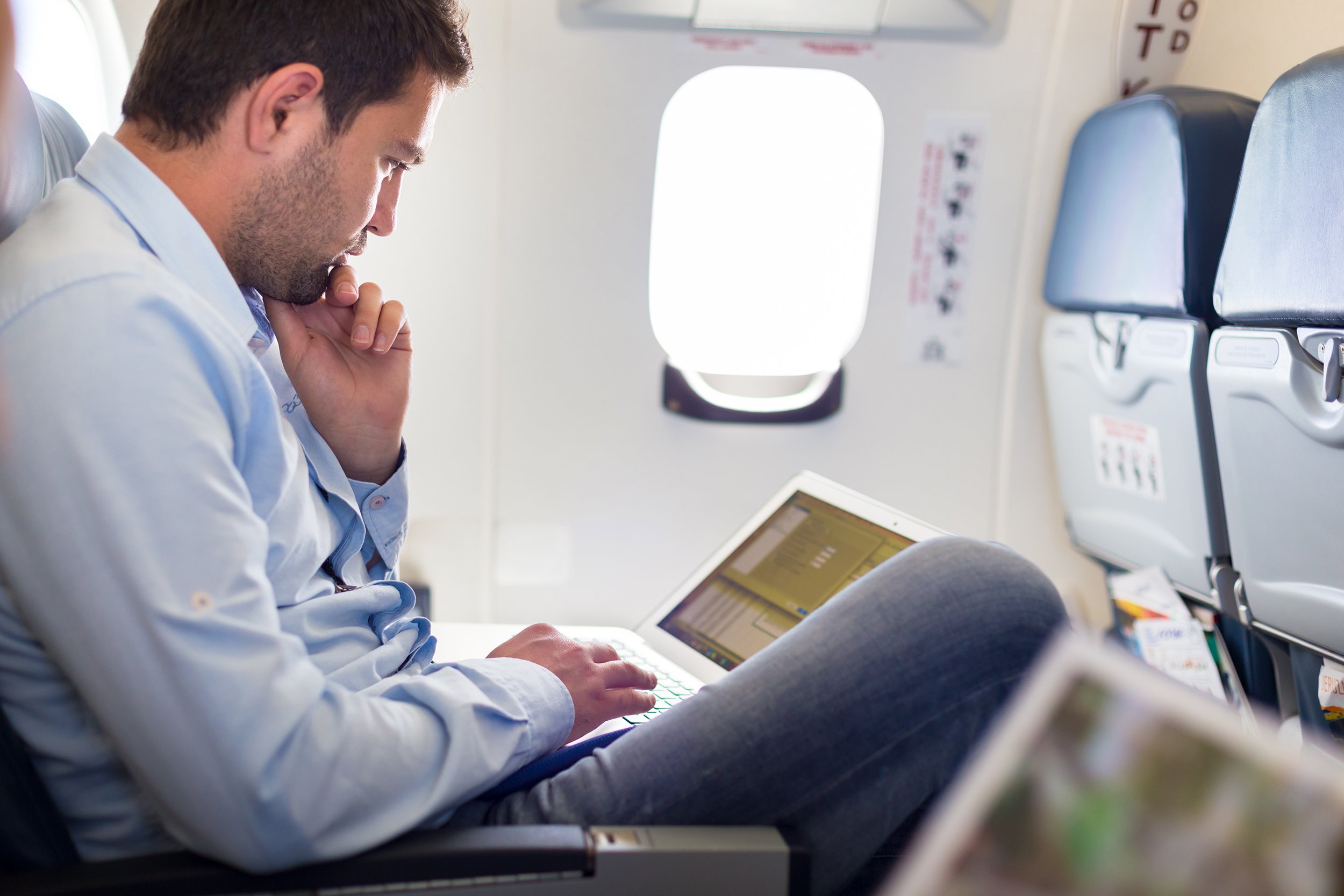 casually dressed middle aged man working on laptop in aircraft cabin