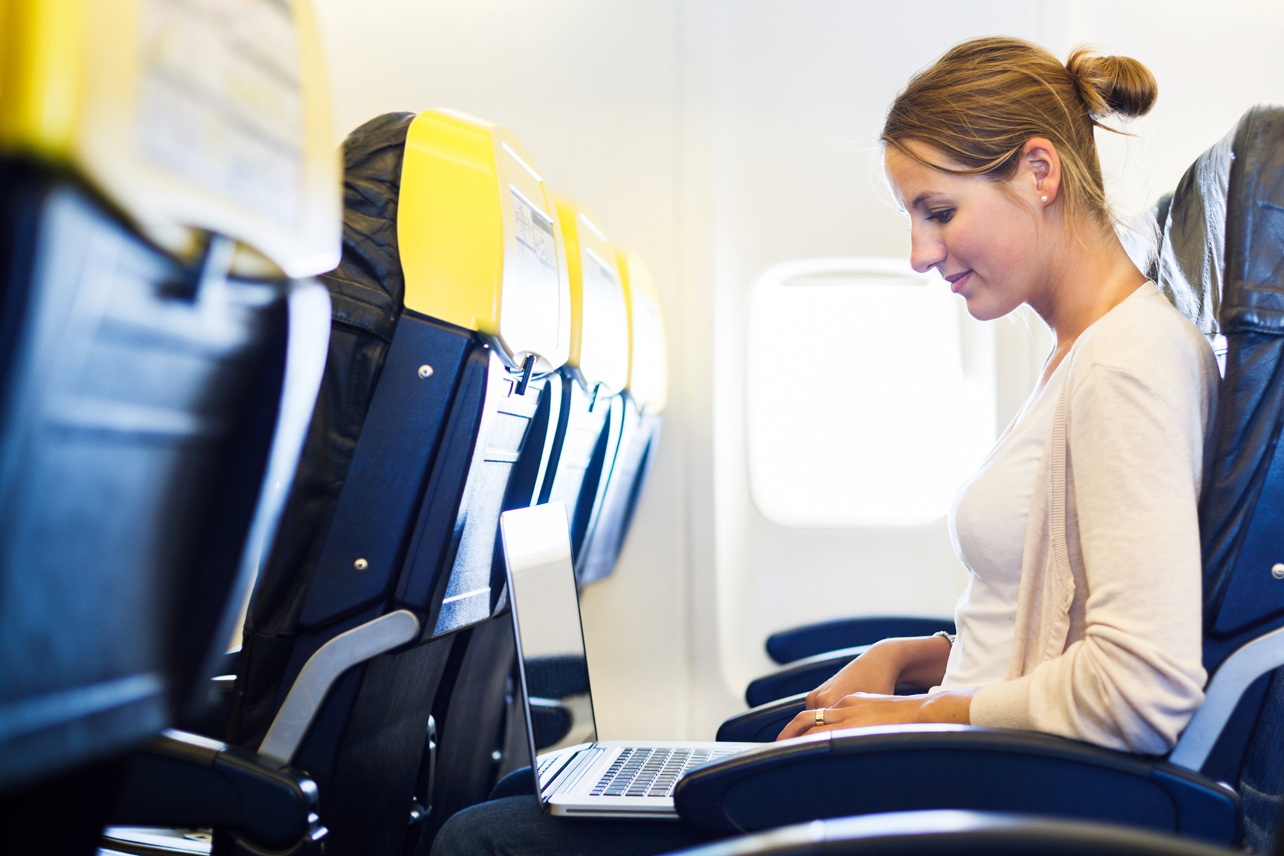 young woman working on her laptop computer on board of an airplane during the flight