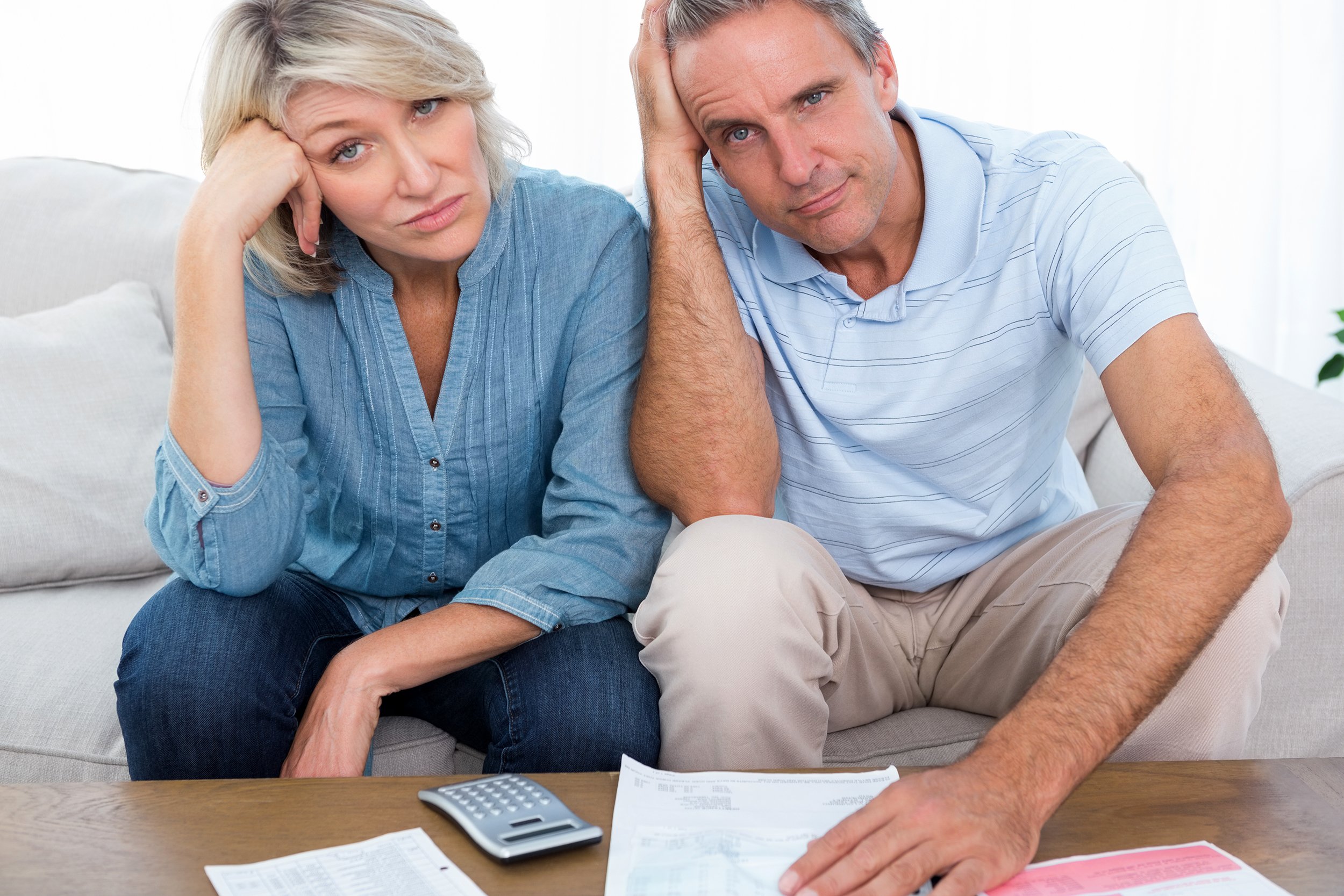 Frustrated older couple sitting at home looking at camera