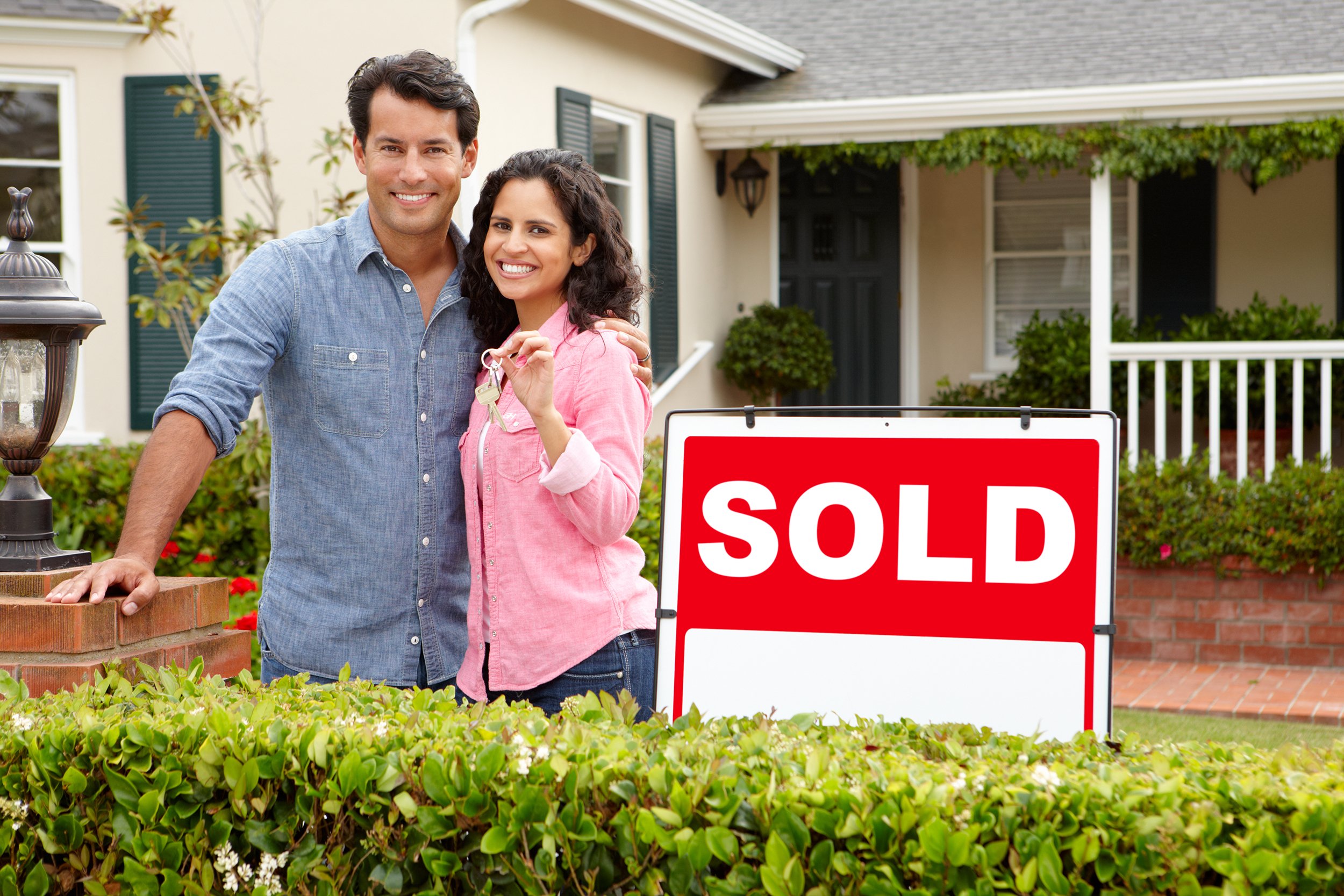 Happy couple outside home with a sold sign