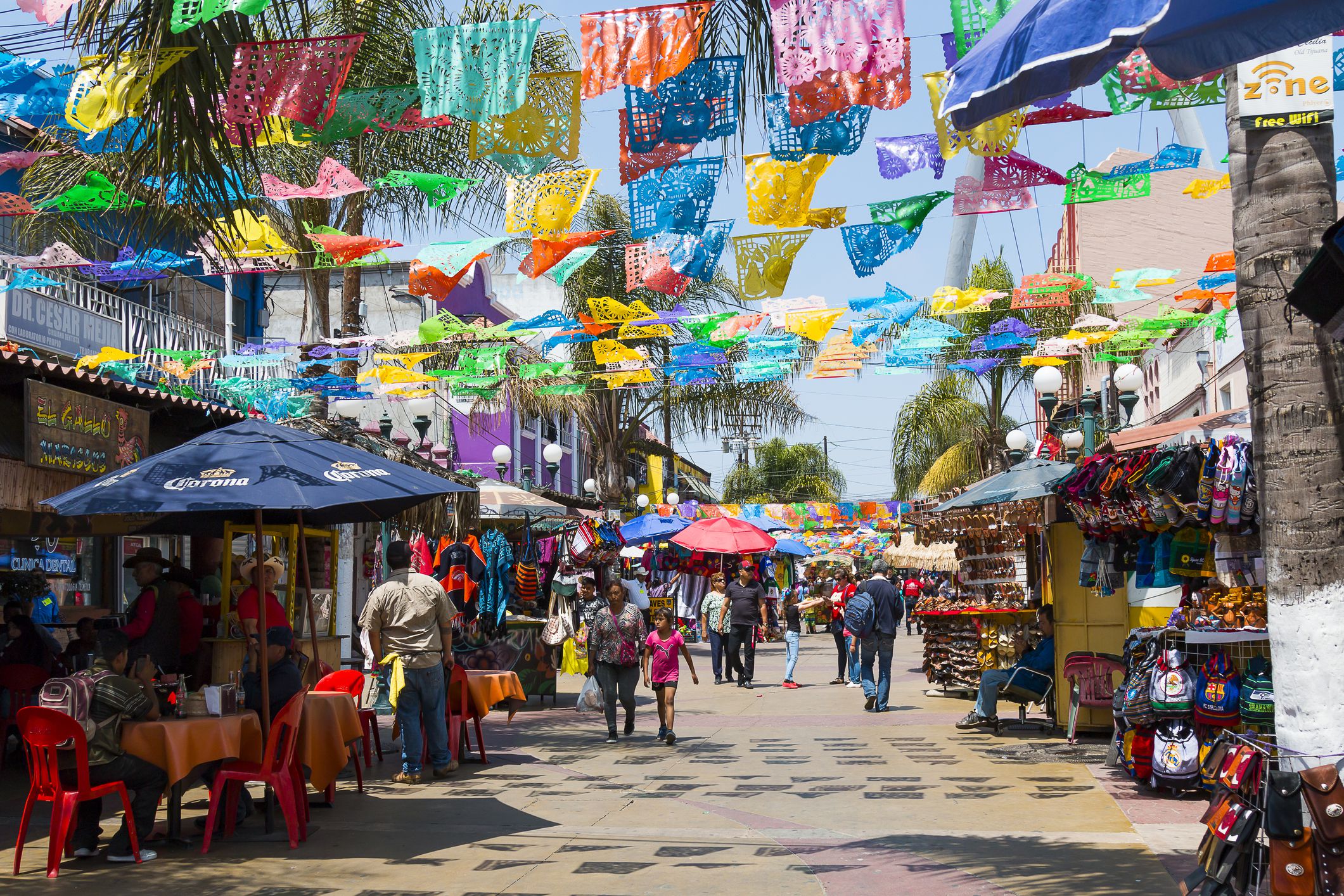 Tijuana, Baja California/Mexico - June 20, 2018: People shop and walk below colorful hanging flags at Plaza Santa Cecilia, a historic Mexican square in the heart of the city.